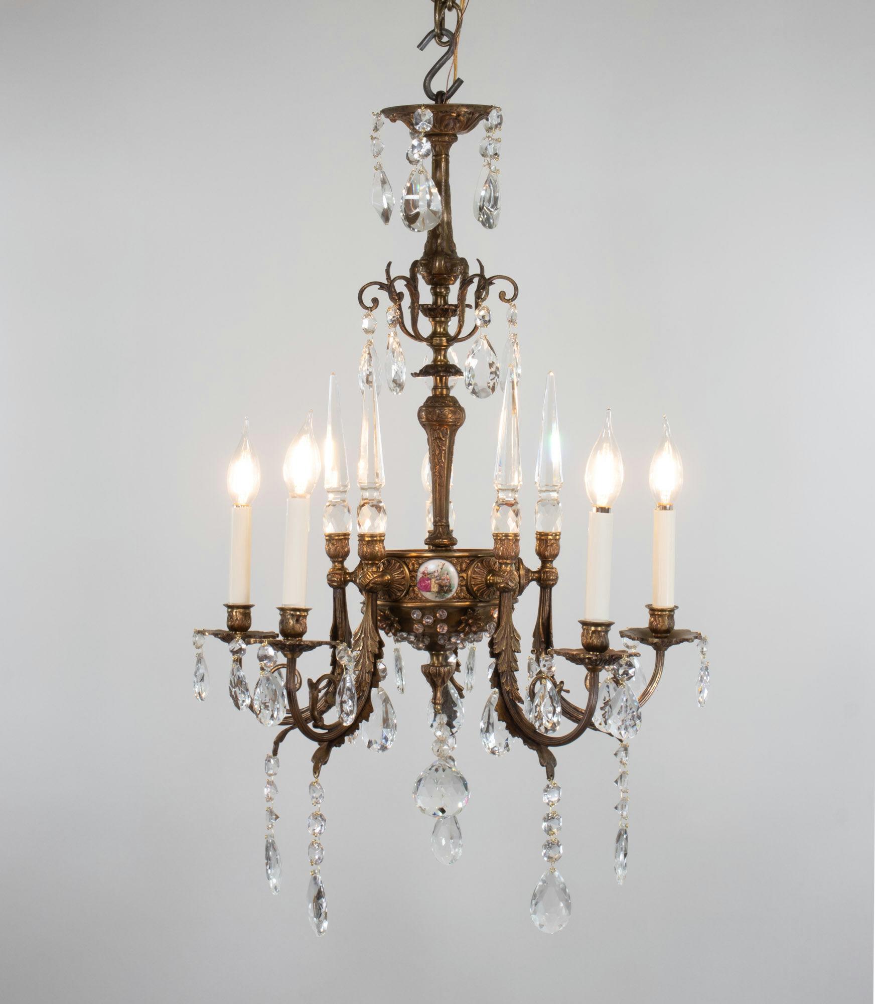Ce lustre en bronze et cristal à cinq branches de style rococo du début du XXe siècle présente des plaques de porcelaine inspirées des œuvres de Jean-Honoré Fragonard, célèbre peintre rococo français. Le style rococo est célébré pour ses éléments