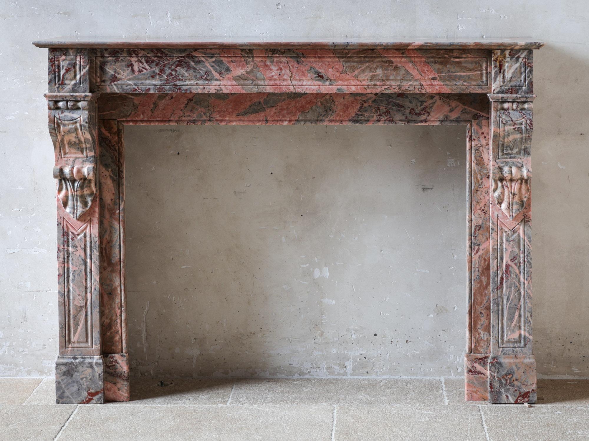 Cette élégante cheminée ancienne, un modèle Modillion, provient de la France du début du 20e siècle et est fabriquée en marbre Sarrancolin exquis. La cheminée en marbre présente une palette sophistiquée de tons à dominante rose et grise, rehaussée