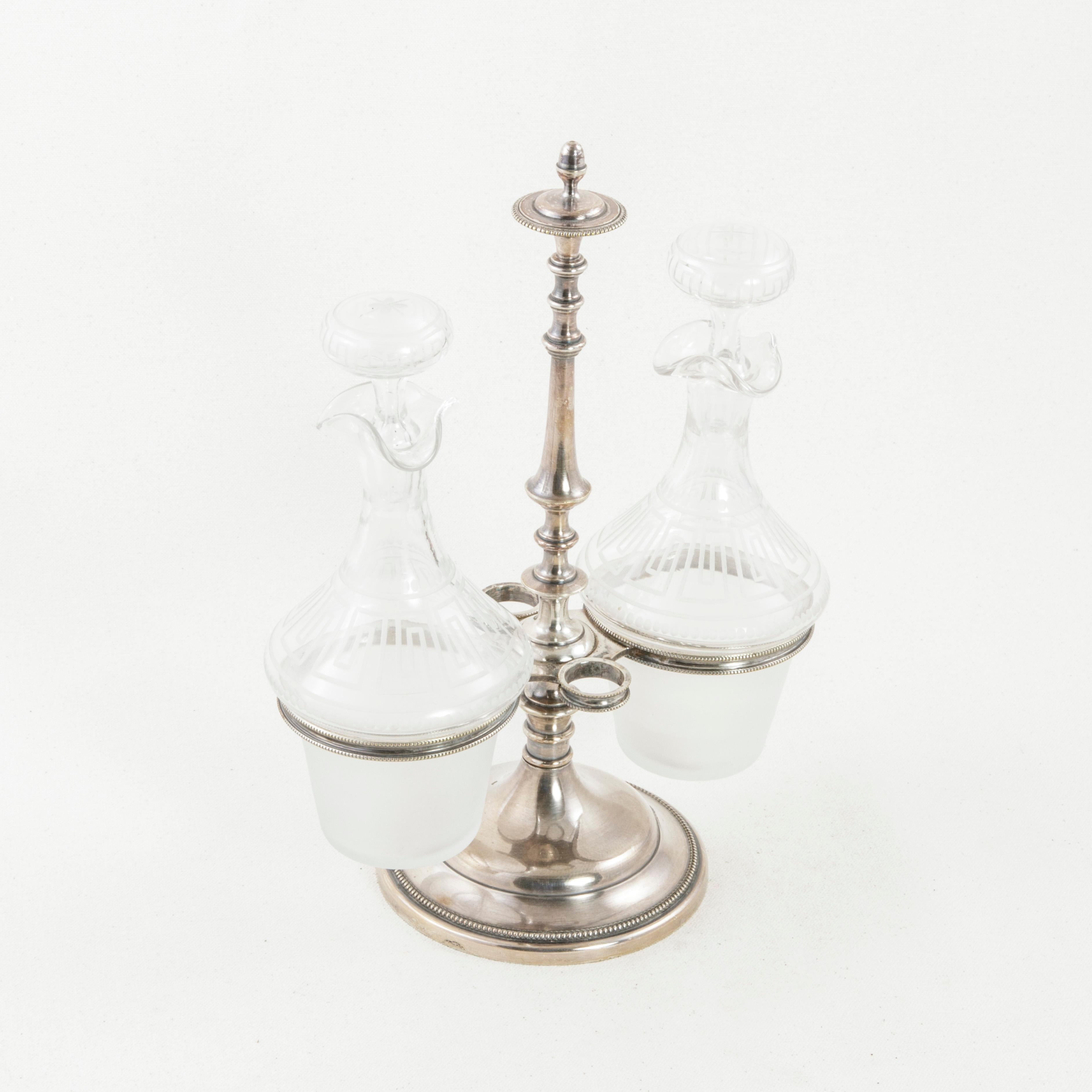 This early 20th century French oil and vinegar cruet set features a footed silver plate support topped with a finial and detailed with beading. Two rings support the crystal carafes containing the oil and vinegar for serving at the table. Additional