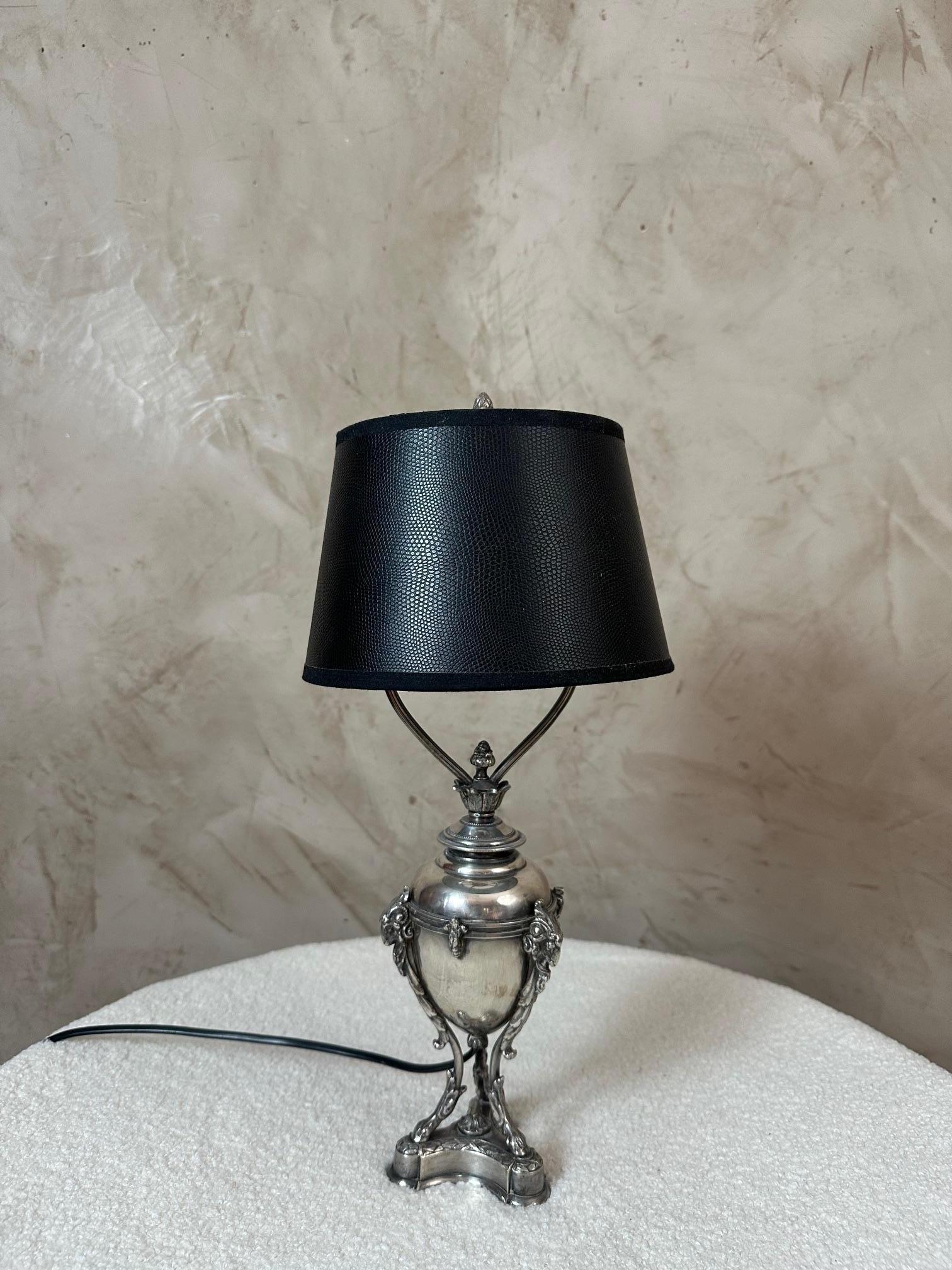Superbe lampe de table argentée, finement travaillée dans un style classique et raffiné. Son socle tripode orné de têtes de bélier et ses lignes élégantes en font une pièce décorative pleine de charme.

Il est complété par un abat-jour noir texturé,