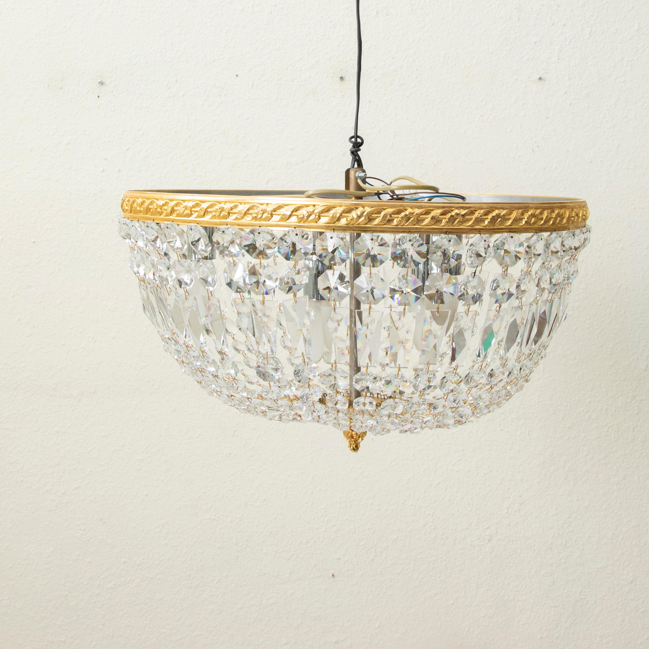 This early 20th century French flush mount chandelier features an upper bronze ring with a twisted ribbon motif. Multi-faceted strings of Strass crystal beading drape to meet a lower brass finial detailed with scrolls. With its large 19.5 inch
