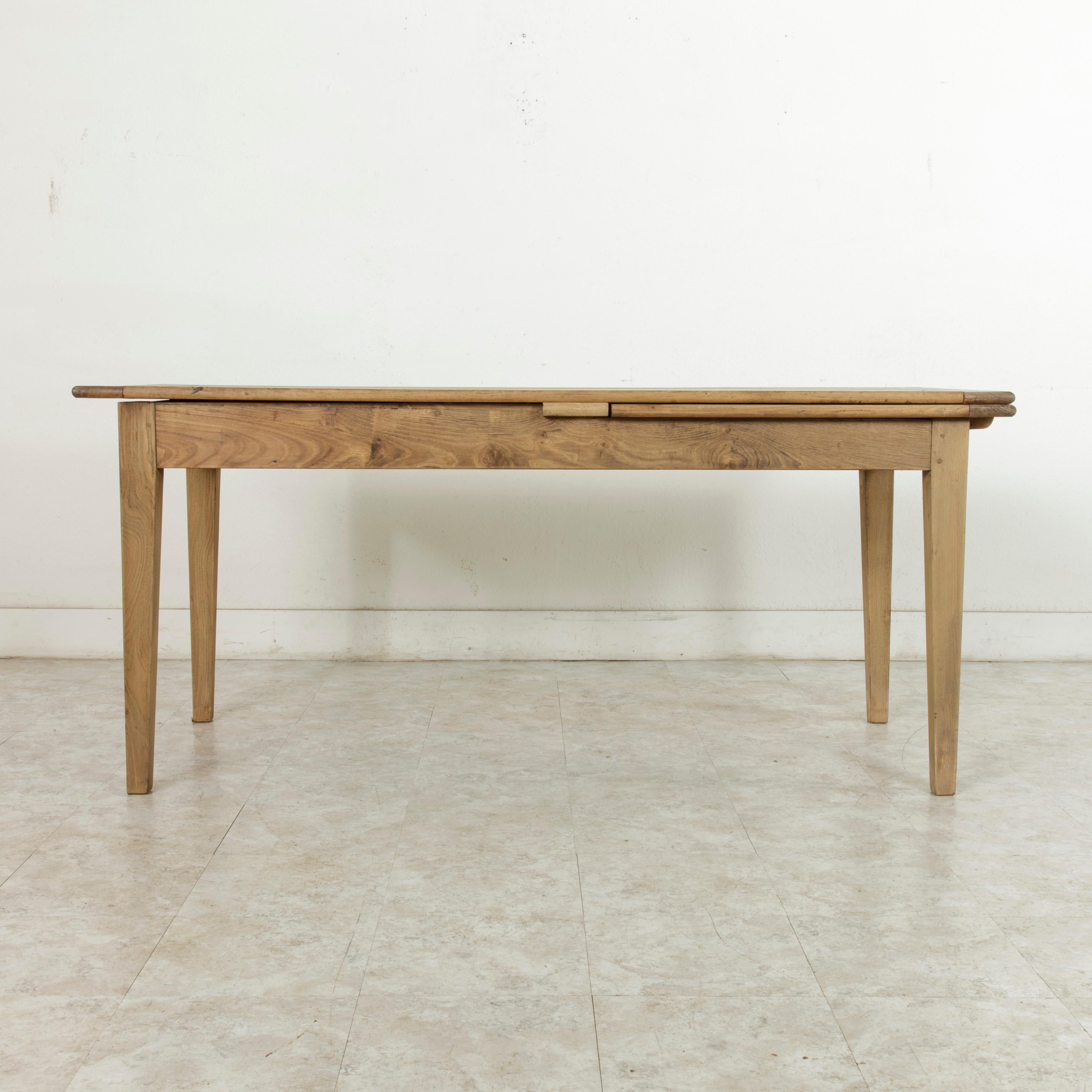 From the region of Le Perche in Normandy, France, this early 20th century oak farm table or dining table features a single draw leaf at one end that pulls out from underneath the tabletop. The pull-out leaf allows the table to accommodate up to