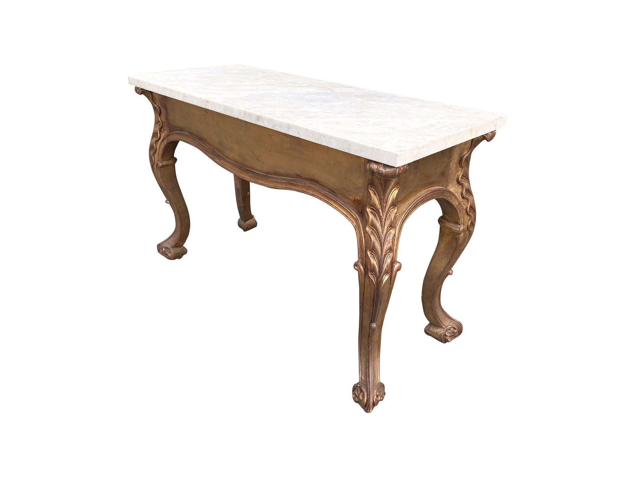 This antique low console table was hand-crafted in the early 20th century. It is comprised of a white marble top and a carved, giltwood base. We particularly love the details of the cabriole legs and how the wood has aged