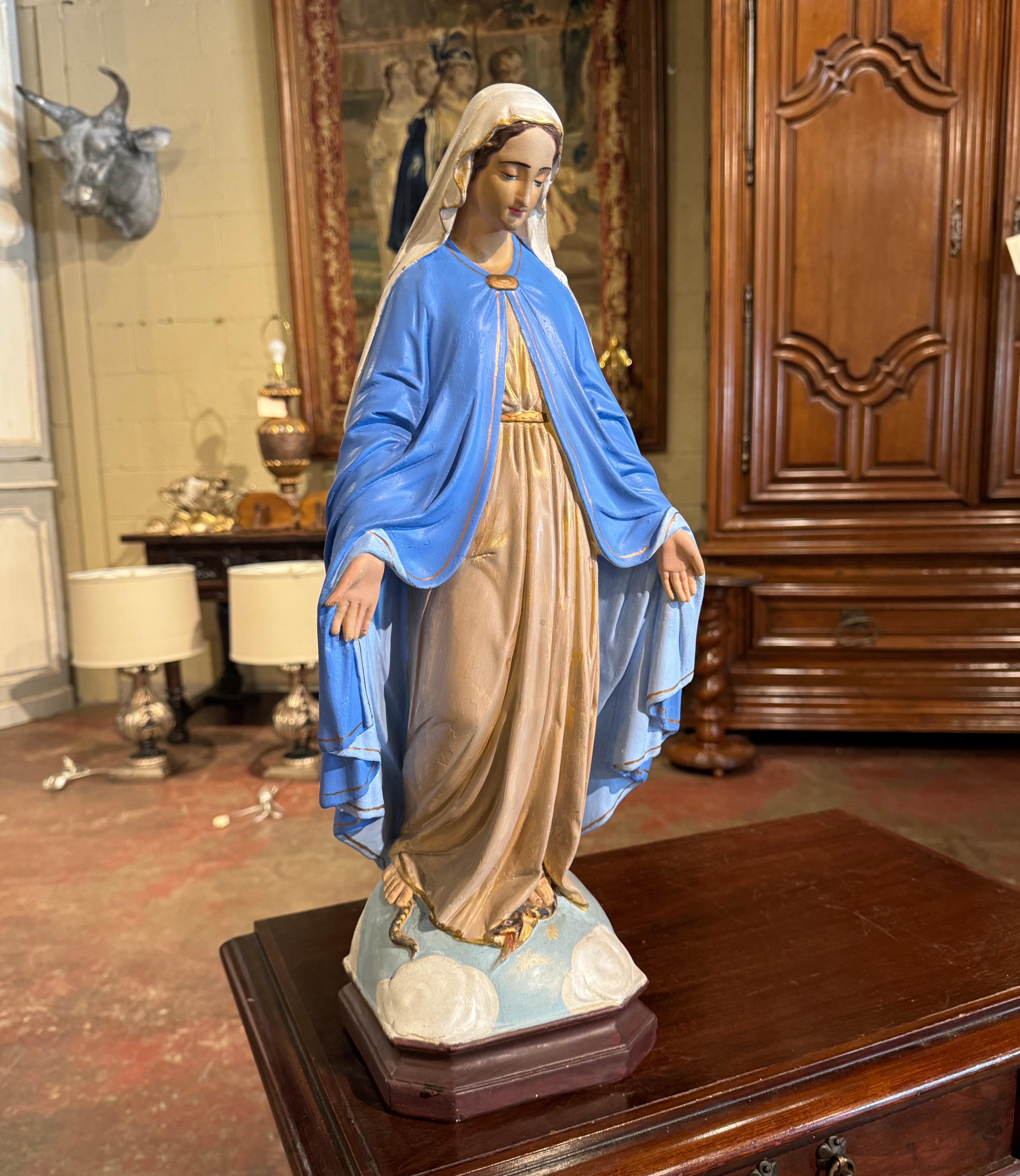 This beautiful and colorful antique Virgin Mary statue was hand carved in France, circa 1920. Built of terracotta, the sculpture depicts our Mother crushing a snake under her foot. The serpent represents Satan, who attempts to tempt and harm