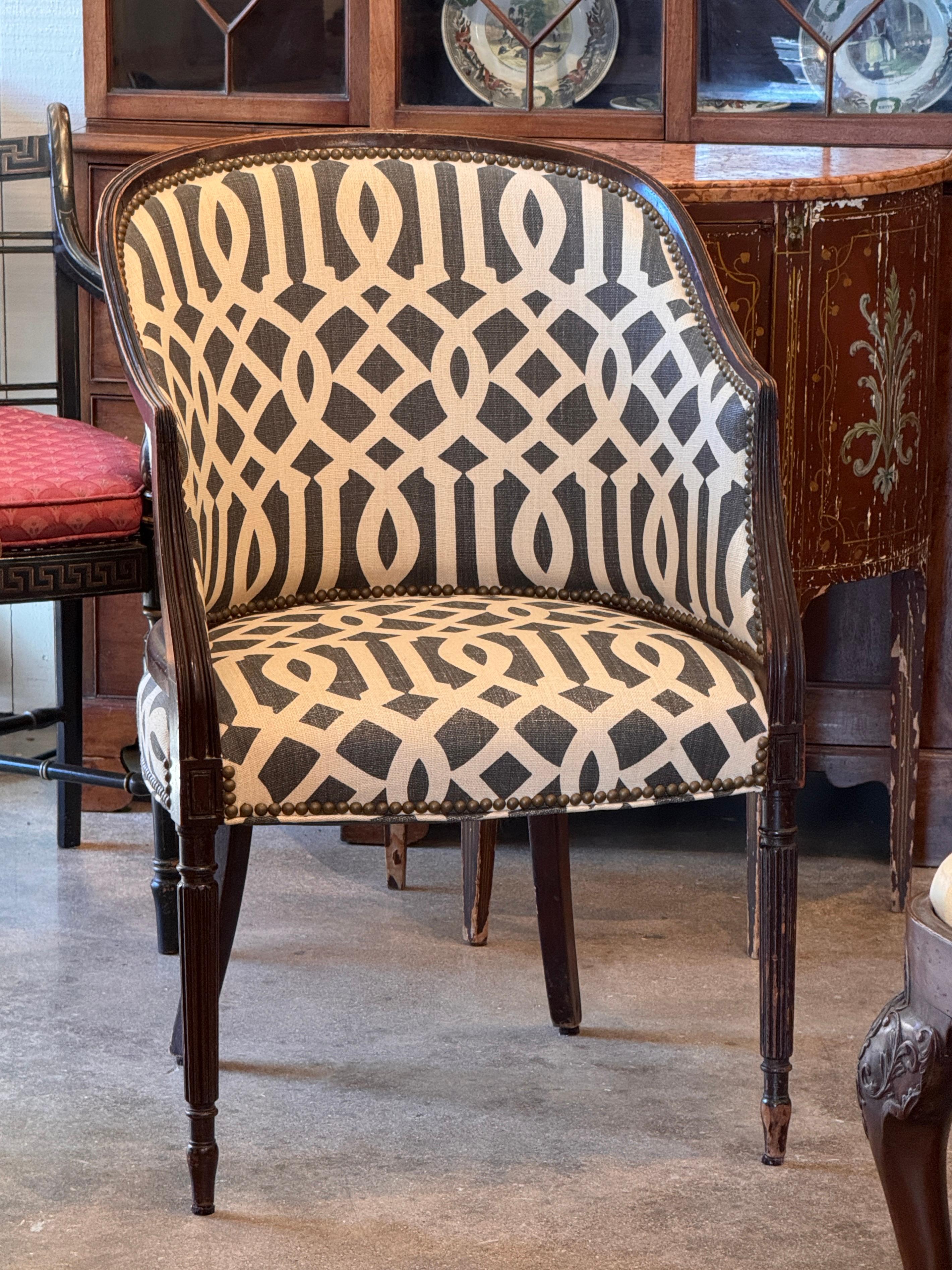 Silla de bañera francesa de principios del siglo XX, con respaldo curvo ajustado, patas delanteras de caña y adornos de latón con clavos. La vista en primer plano destaca la tapicería geométrica actualizada y los limpios detalles de los bordes a lo