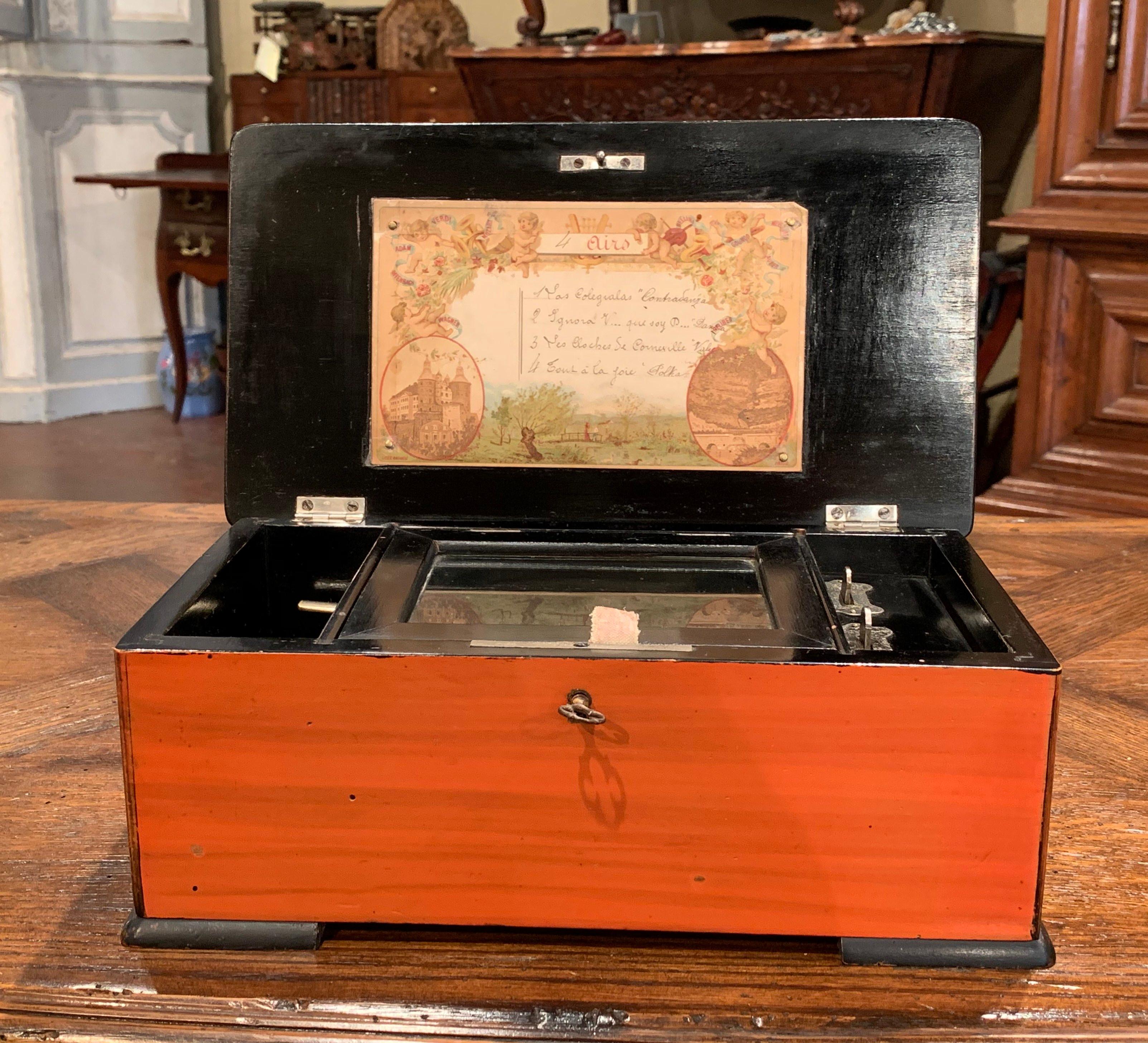Hören Sie mit dieser traditionellen, antiken Spieluhr sanfte, fröhliche Musik in Ihrem Wohnzimmer. Das um 1900 in Paris, Frankreich, gefertigte Tulpenholzgehäuse mit eingelegtem Messingdekor hat schwarz lackierte Kanten und ein handgemaltes