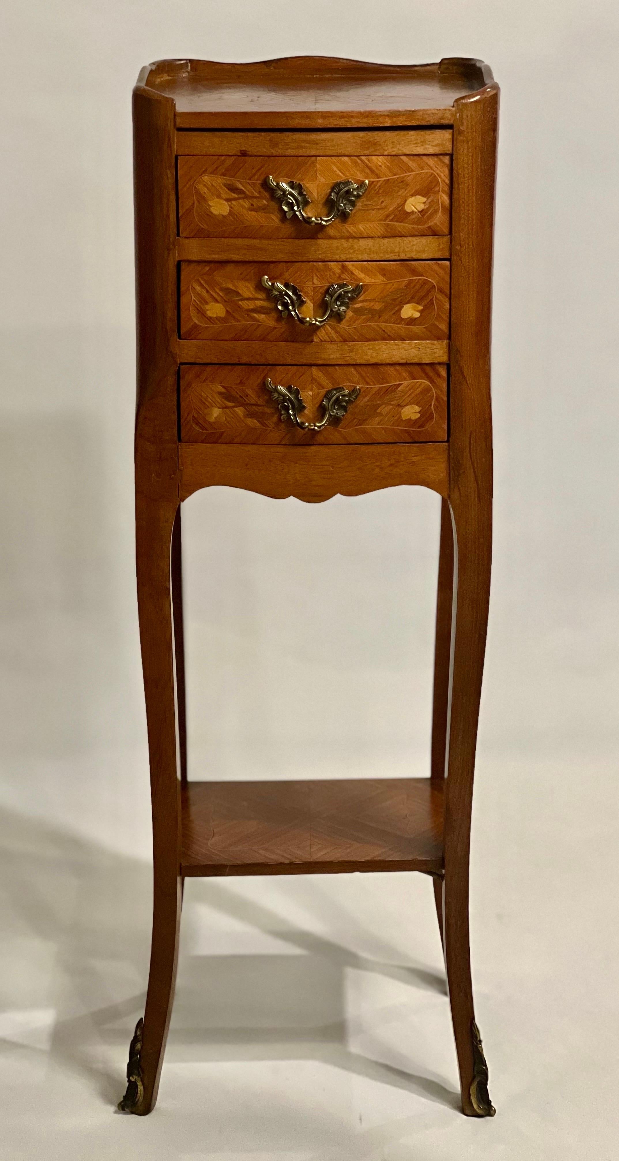 Petite French Louis XV style three-drawer side table or bedside stand, c. early 20th century.

Beautiful stand in tulipwood with marquetry on the top, sides and front. The tray style top and drawers feature a satinwood inlay with floral detail and
