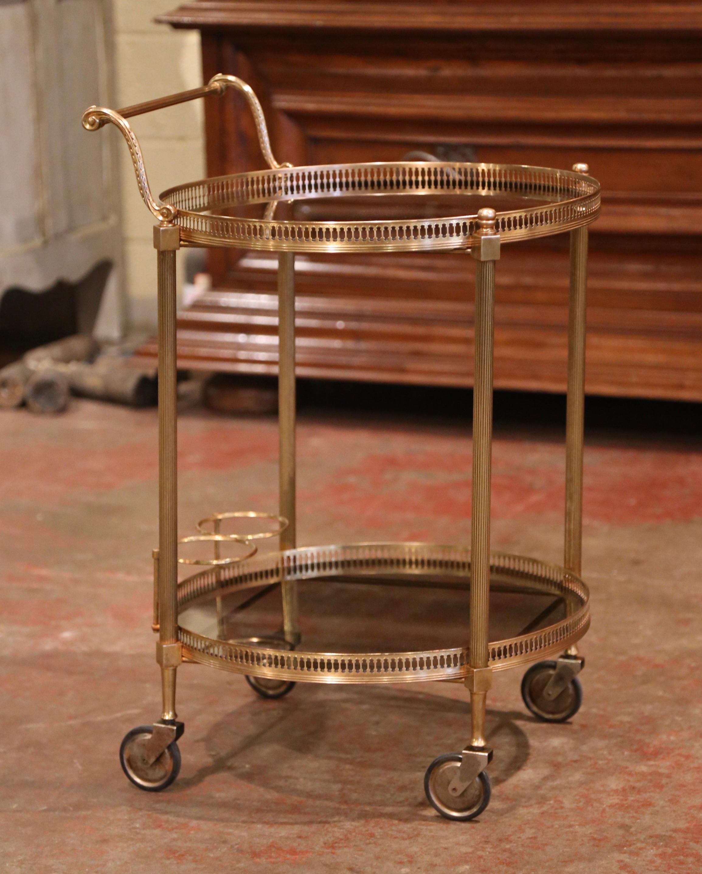 This elegant vintage rolling cart was created in France, circa 1930, the brass bar table stands on small round wheels over four straight spline legs decorated at the center. The cart features two plateaus both topped with tainted glass surfaces; the