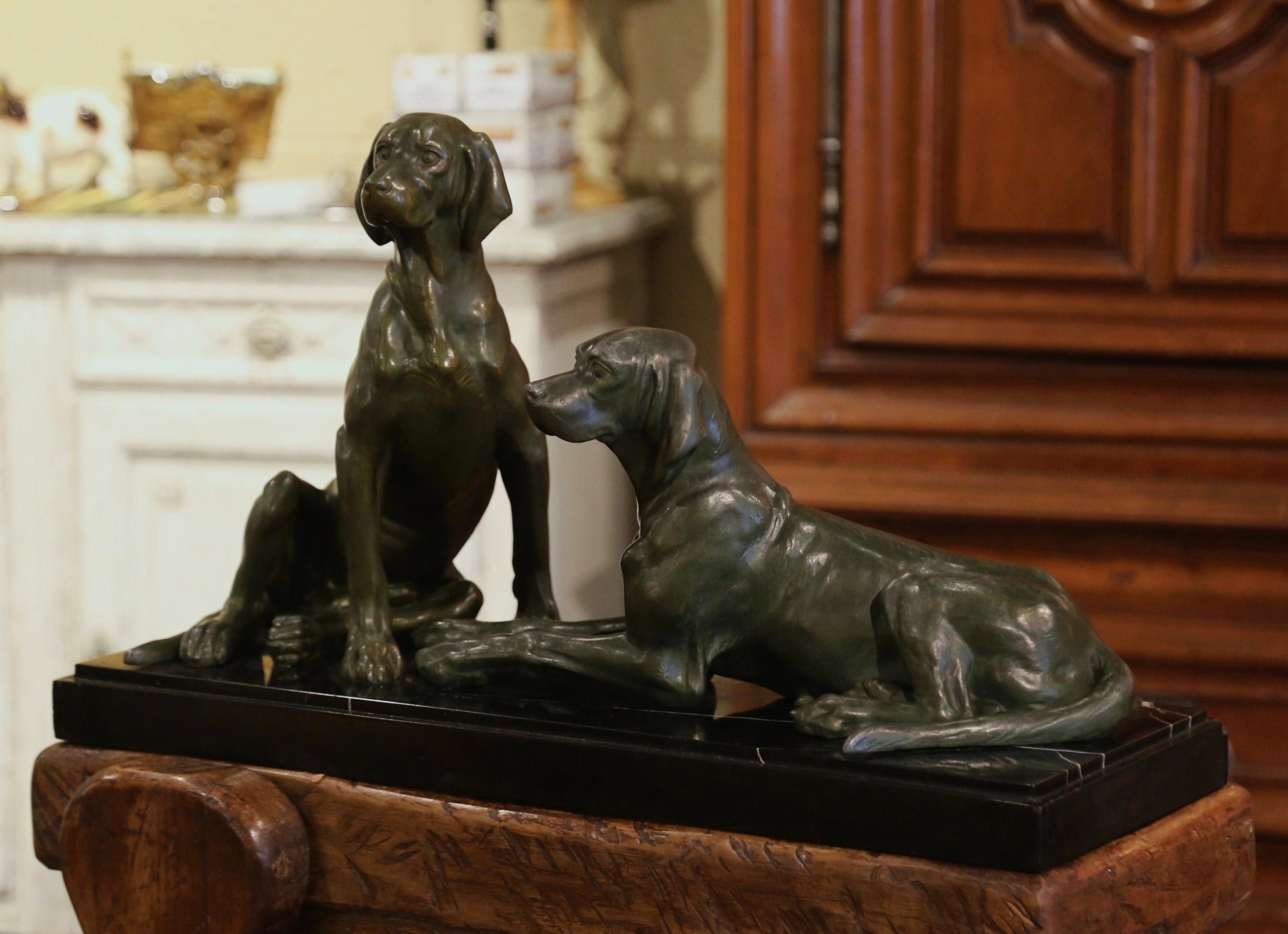 Cette composition de sculpture de chien antique a été créée en France, vers 1920. Posée sur un socle en marbre noir, la composition représente un couple de fiers labradors, tous deux au repos, l'un sur ses pattes arrière, l'autre couché. Cette