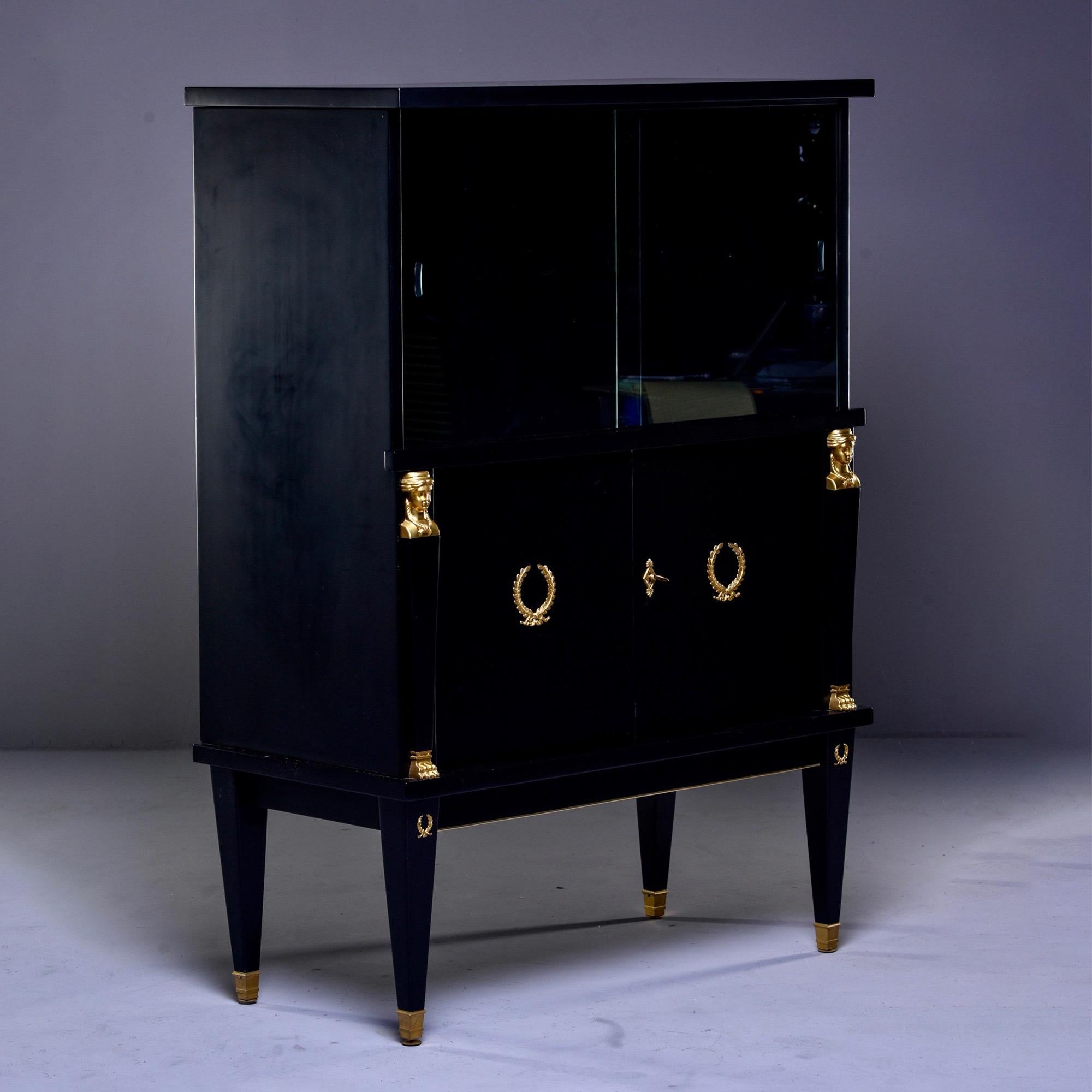 French vitrine cabinet or dry bar with new black finish and original brass trim, circa 1920s. Top has sliding glass doors. Bottom has brass figural ornaments, locking door and single internal shelf. Tapered legs with brass capped feet. Unknown maker.