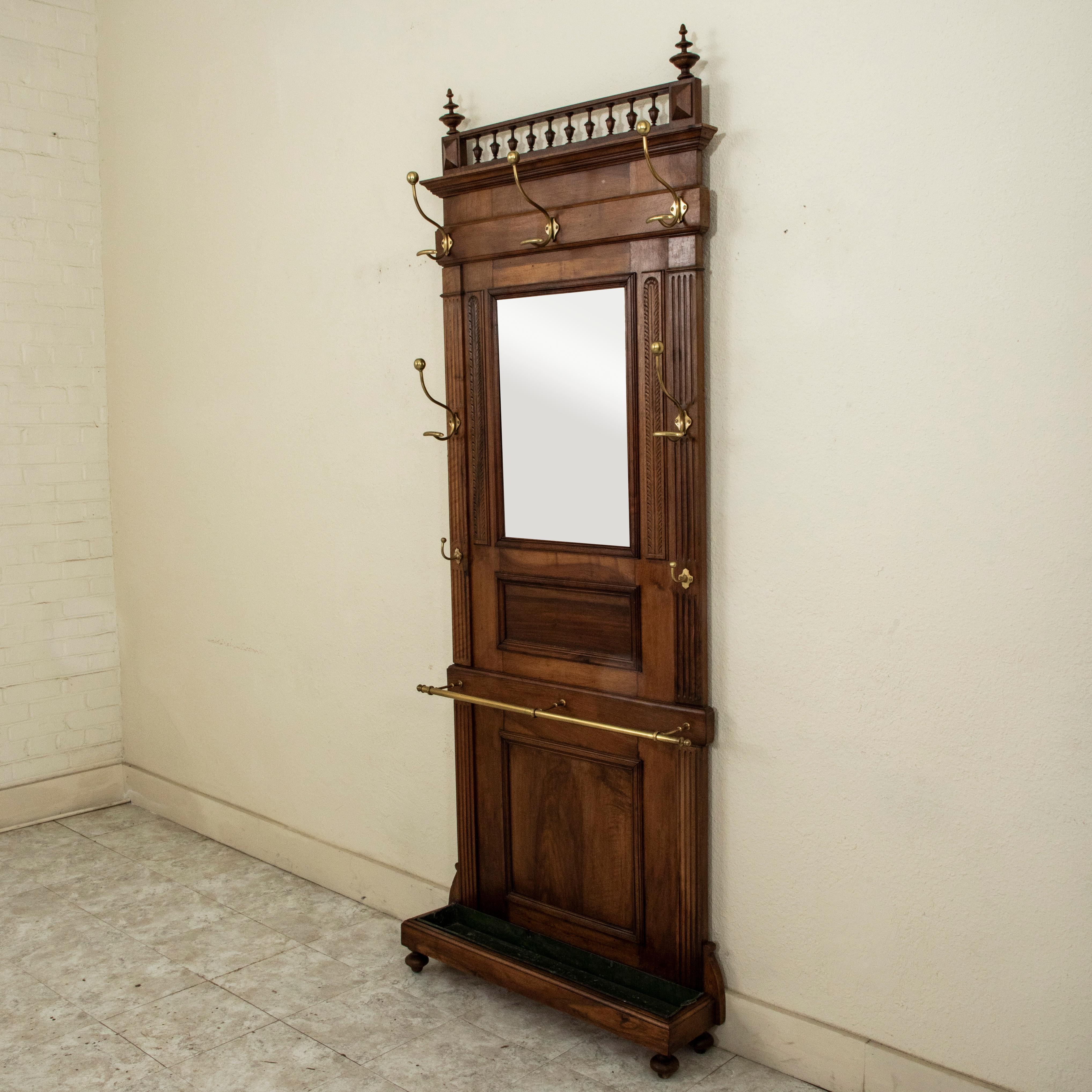 This early twentieth century Henri II style hall tree is constructed of solid walnut with seven bronze hooks and its original beveled mirror. It is detailed with fluting on the sides, a stylized leaf pattern, and a removable upper banister with