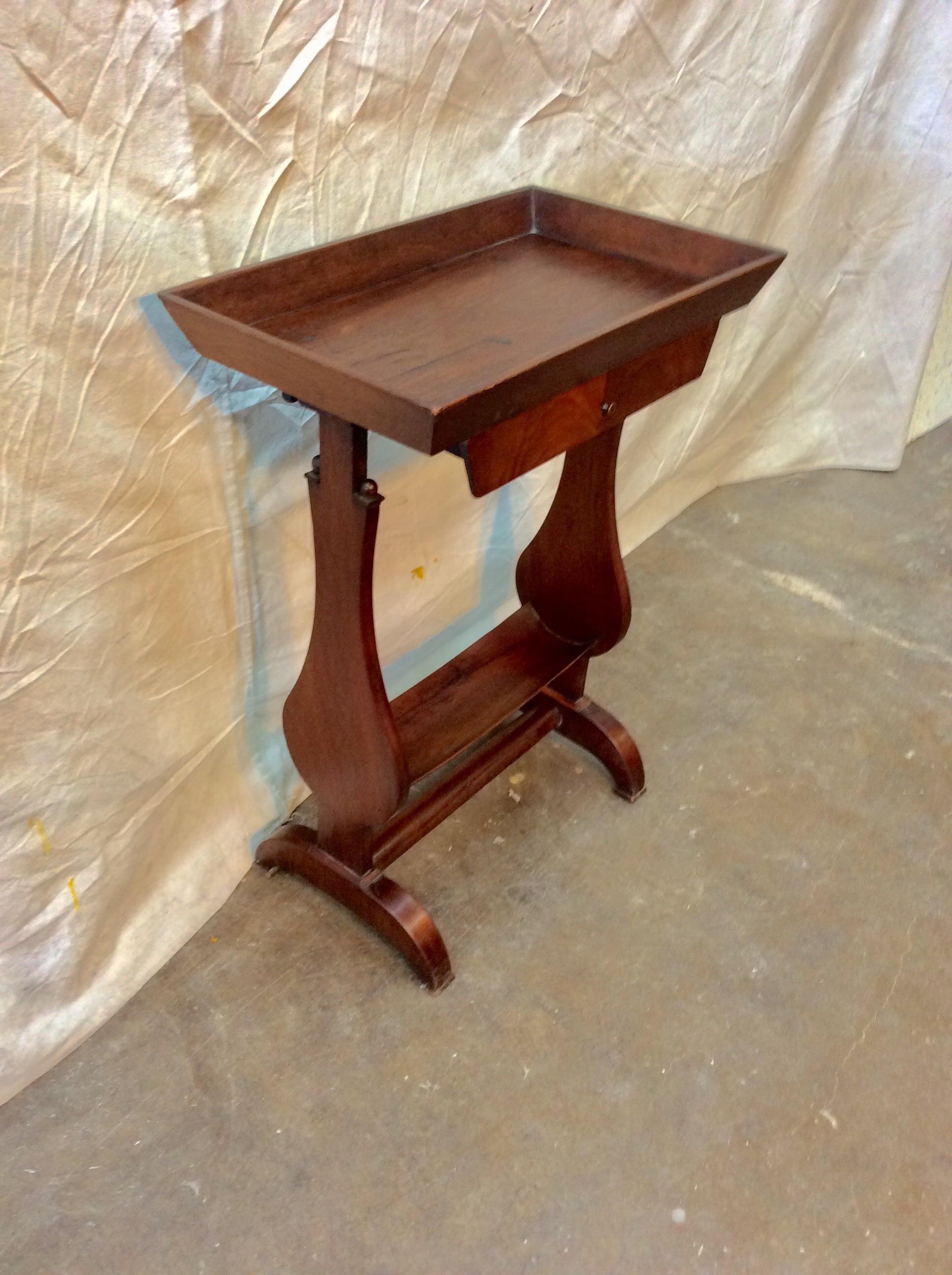 Found in the South of France, this petite Early 20th century French Walnut Side Table is crafted with a raised edge top, one drawer adorned with a brass pull and a storage space on the bottom, possibly for a book or magazine. The two shapely carved