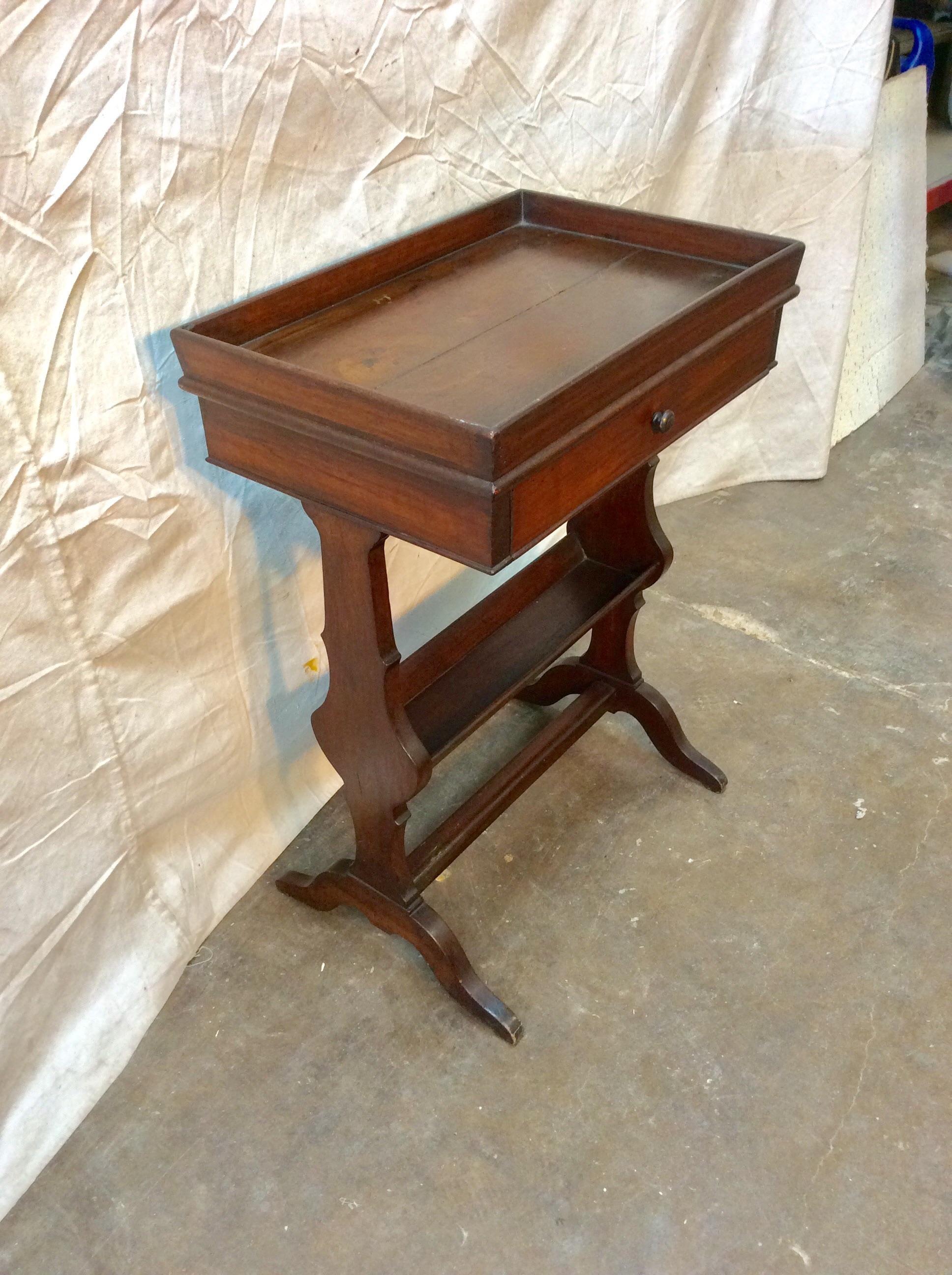 Found in the South of France, this petite early 20th century French Walnut Side Table is crafted with a raised edge top, one hand dovetailed drawer adorned with a wood pull and a storage space on the bottom, possibly for a book or magazine. The two