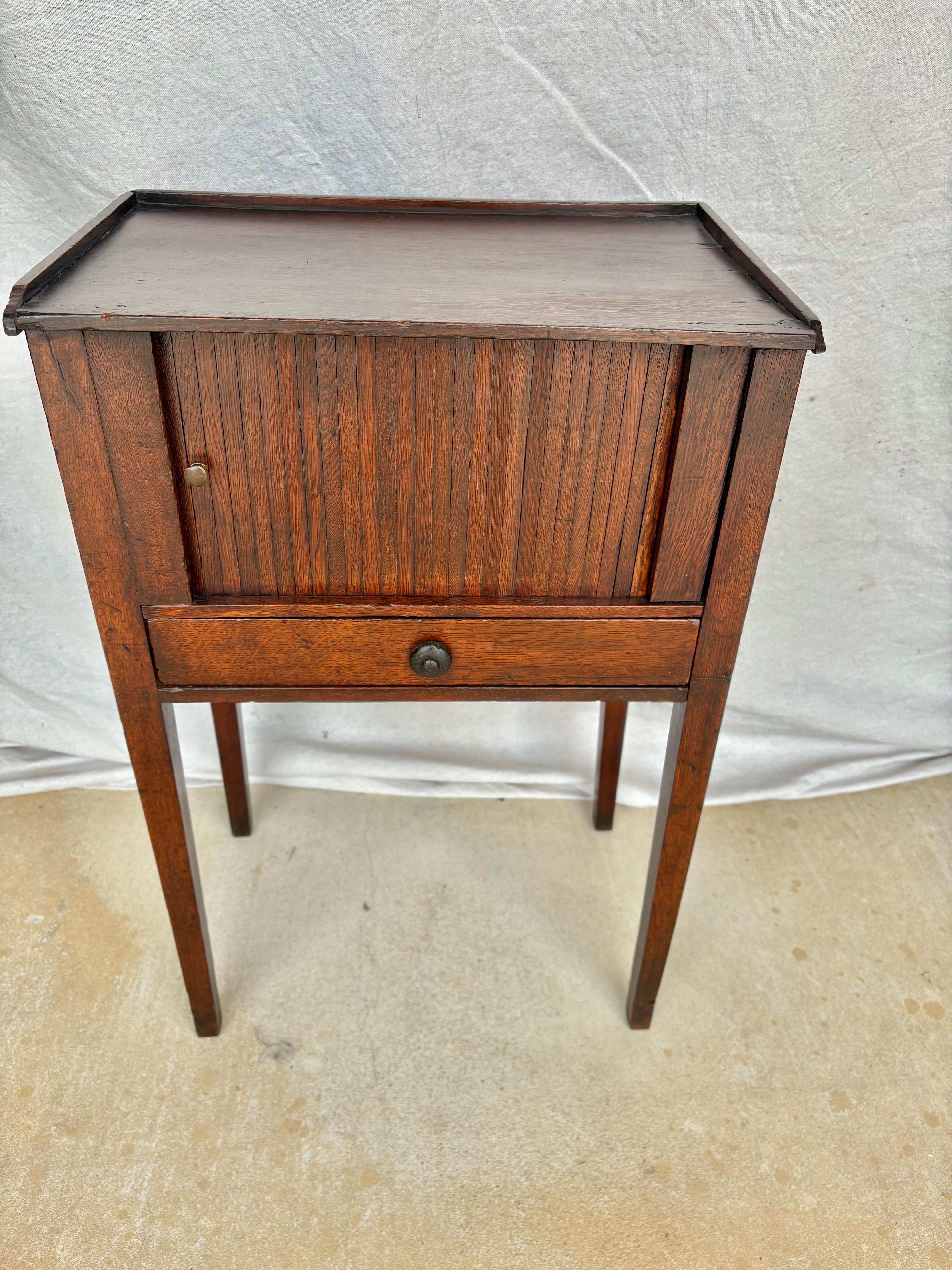 Found in the South of France, this Early 20th Century French Side Table was crafted from old growth walnut in the early 1900's.  The piece features a raised edge top on three sides resting above a tambour style sliding door that opens to reveal a