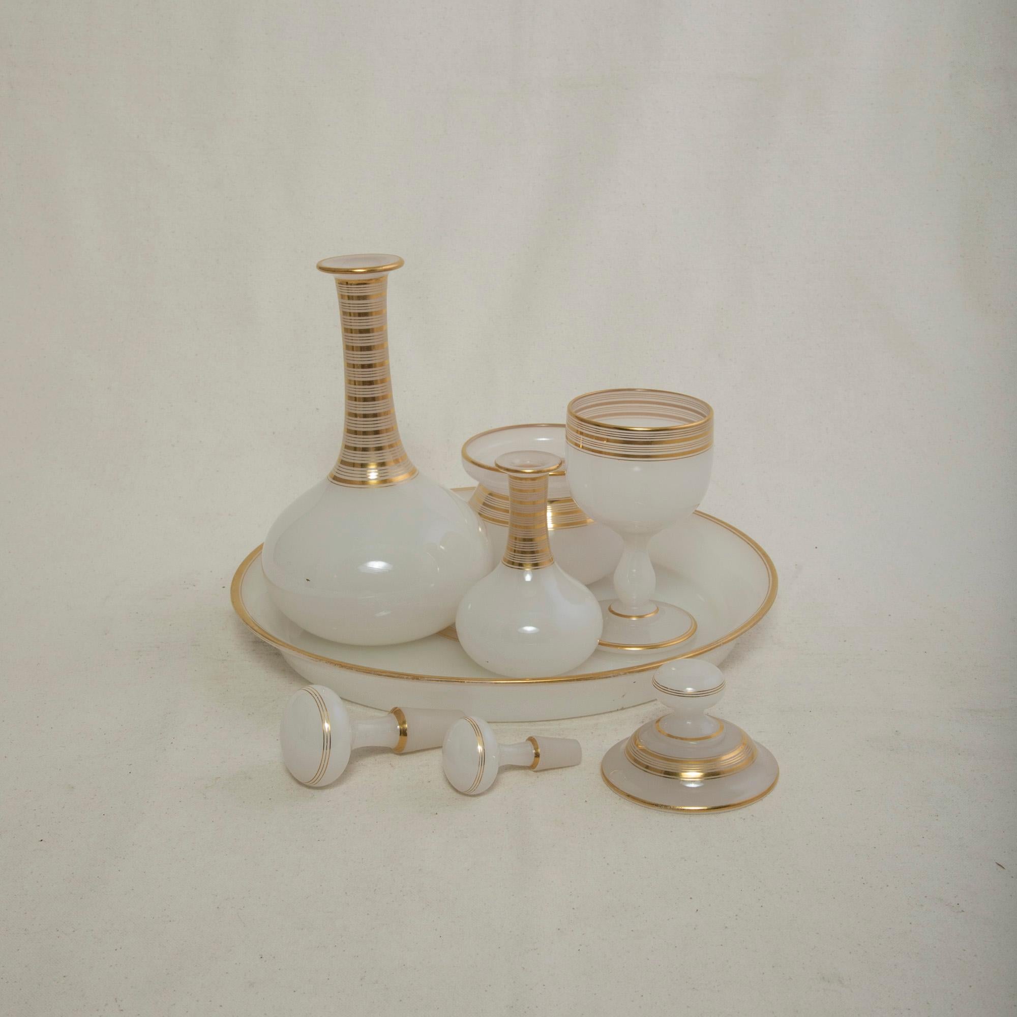 This turn of the twentieth century French opaline vanity set includes a tray, goblet, a bowl with lid, and two bottles with their stoppers. Each piece is detailed with concentric rings of gold. The tray measures 1.5 inches high by 11 inches in