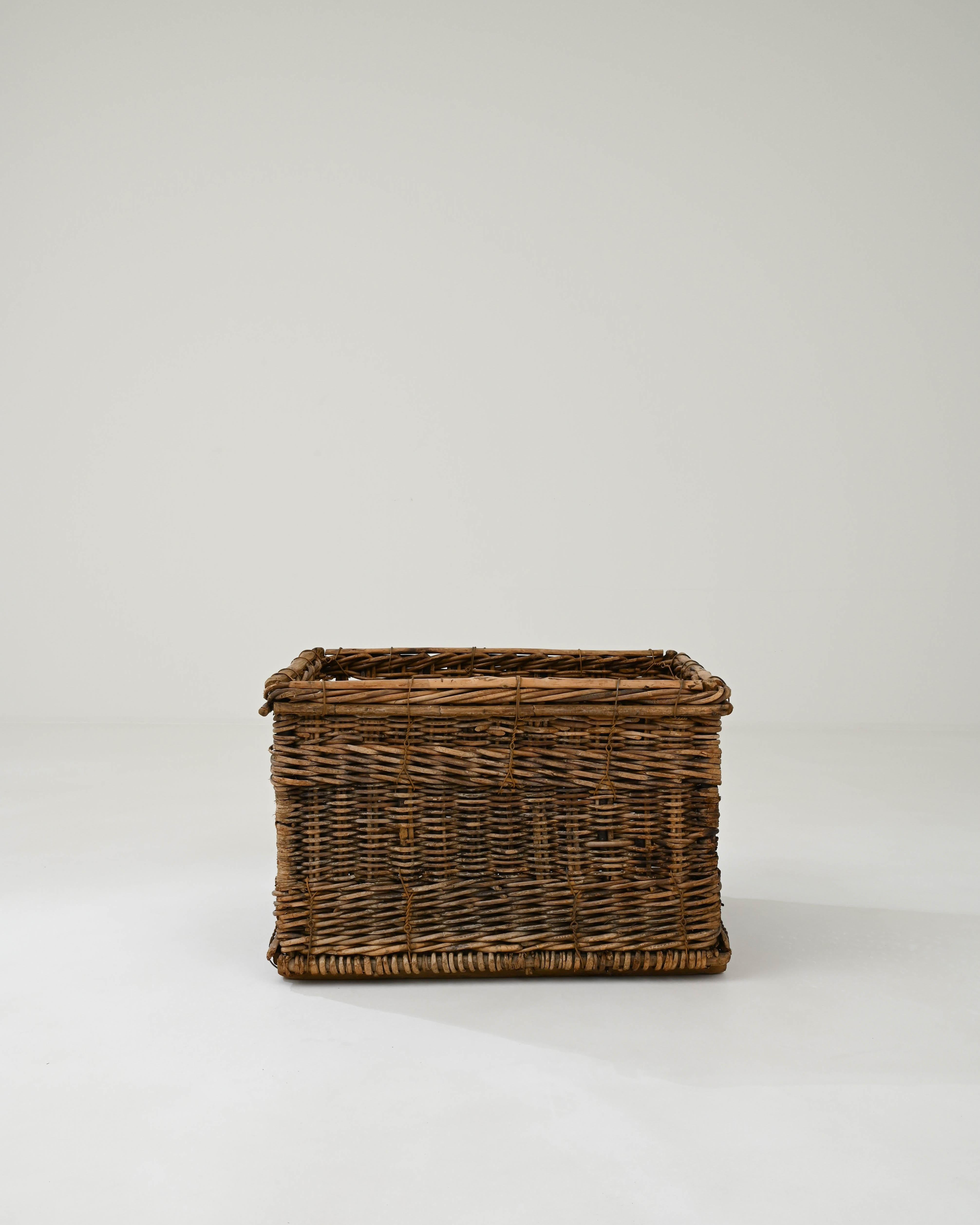 Hand-woven in France in the early 20th century, this wicker basket boasts a practical rectangular shape and the craftsmanship of the weaving technique, imparting a sense of rustic coziness. This unique basket is interwoven with a metal wire