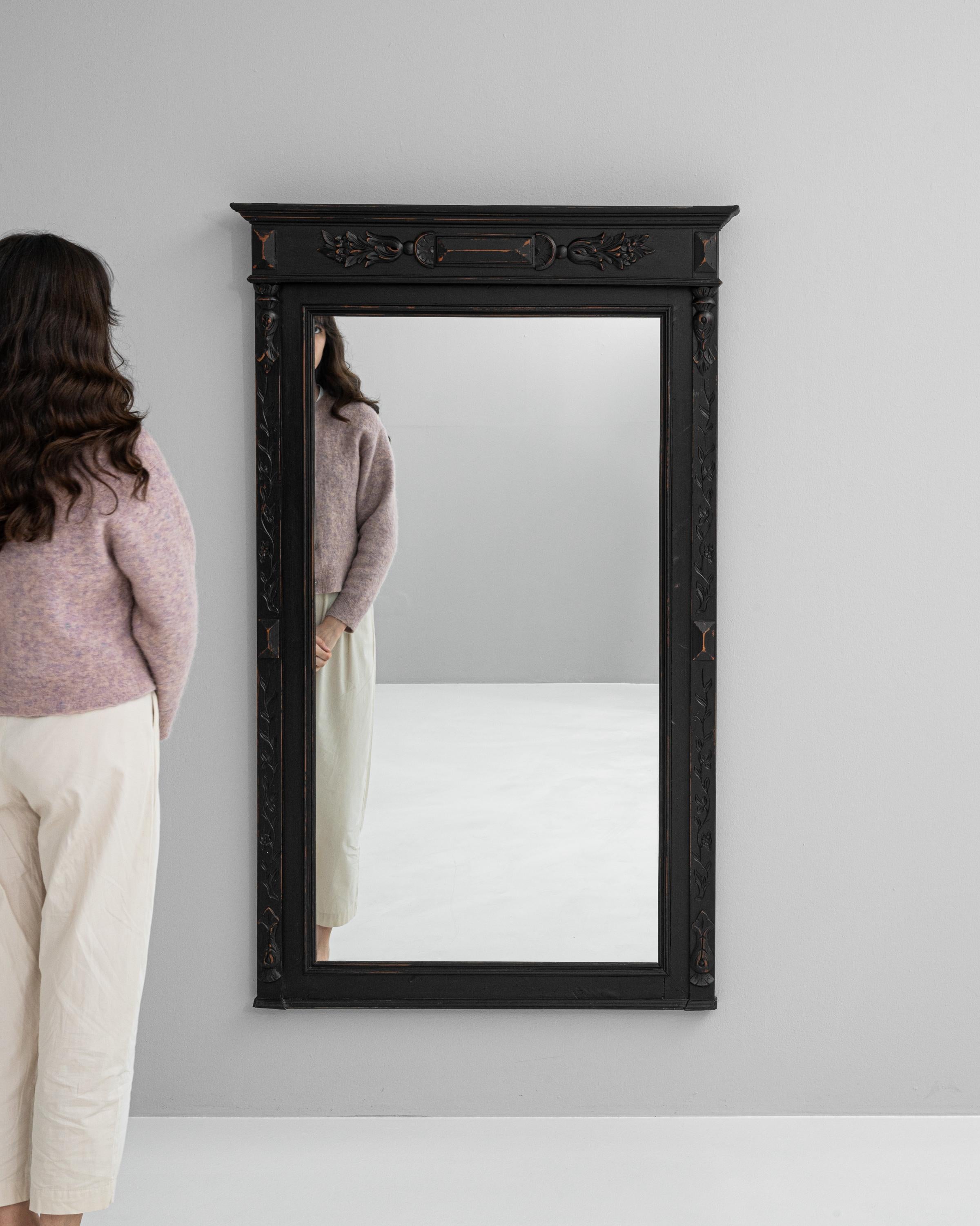 Mit diesem schwarz patinierten Spiegel aus französischem Holz des frühen 20. Jahrhunderts versetzen Sie sich in den Charme vergangener Zeiten. Dieser Spiegel wurde in einer Zeit gefertigt, in der die Liebe zum Detail an erster Stelle stand. Er zeigt
