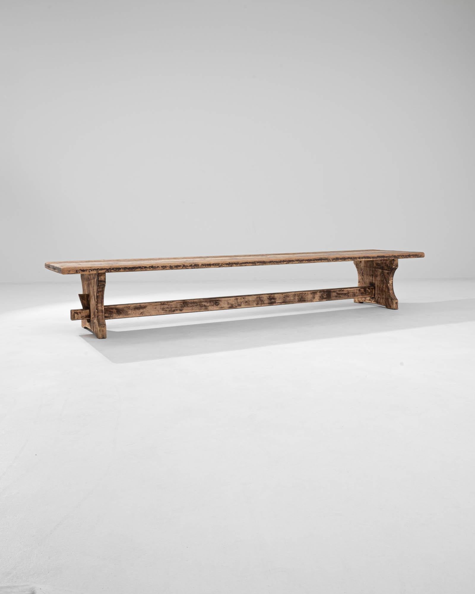 A simple shape combined with a timeworn patina make this Provincial wooden bench an attractive find. Built in France in the early 20th century, a long seat of wooden boards rests atop trestle legs, joined by a stretcher. Mortise and tenon joints