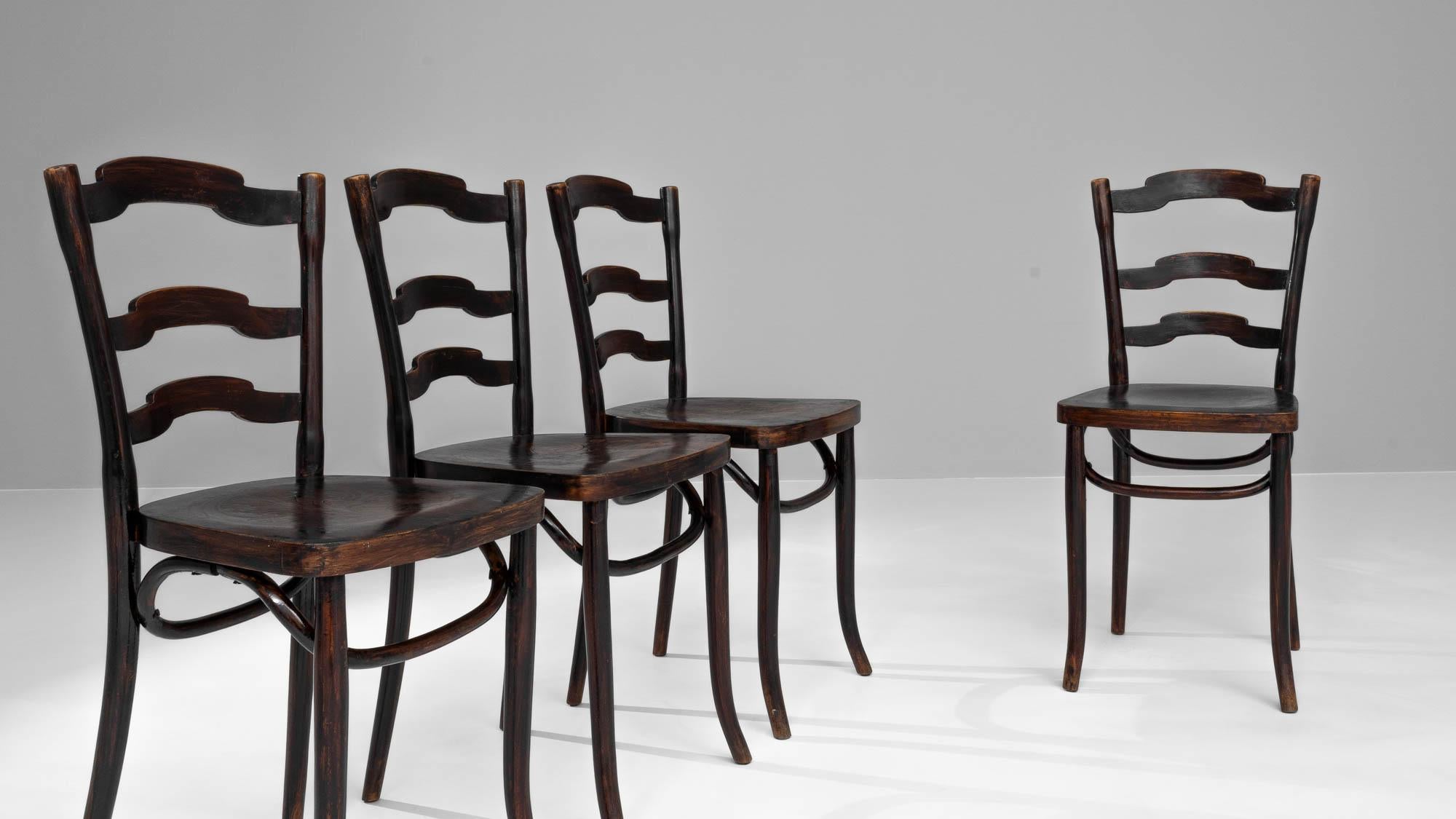 Remontez le temps avec cet ensemble exquis de quatre chaises de salle à manger françaises en bois du début du 20e siècle, un ajout classique à toute salle à manger. Chaque chaise a été méticuleusement fabriquée et bénéficie d'une riche finition en