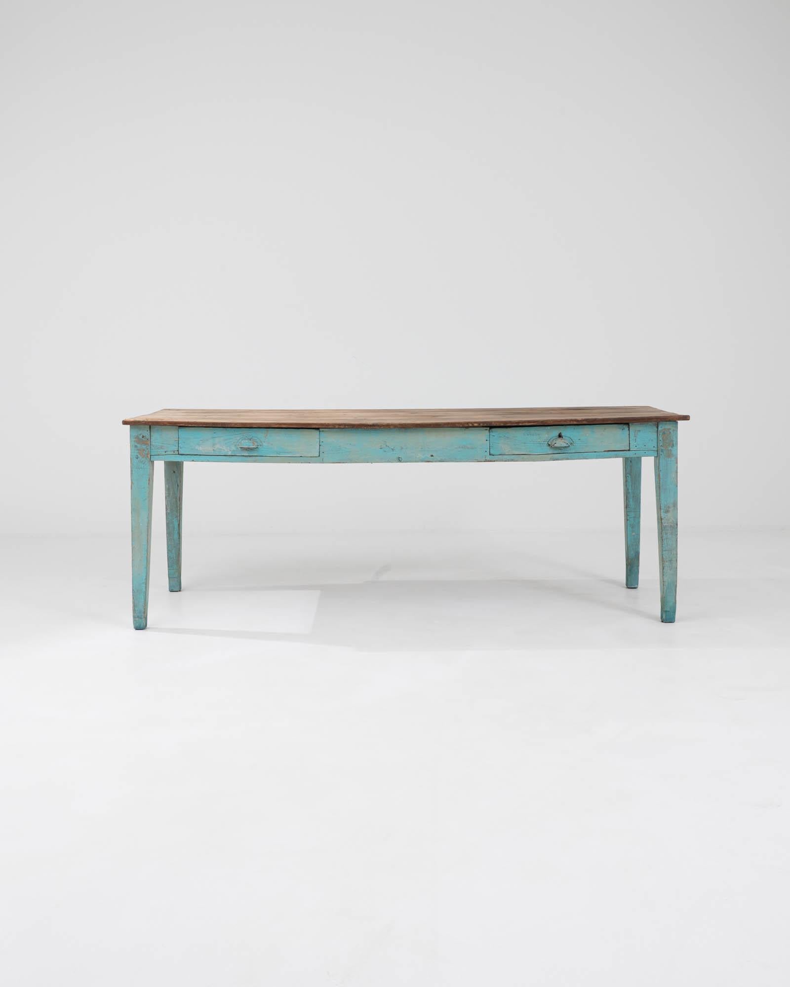 Introducing our exquisite Early 20th Century French Wooden Dining Table, a captivating fusion of vintage charm and timeless elegance. Crafted with meticulous attention to detail, this dining table boasts a unique aquamarine-colored base that adds a