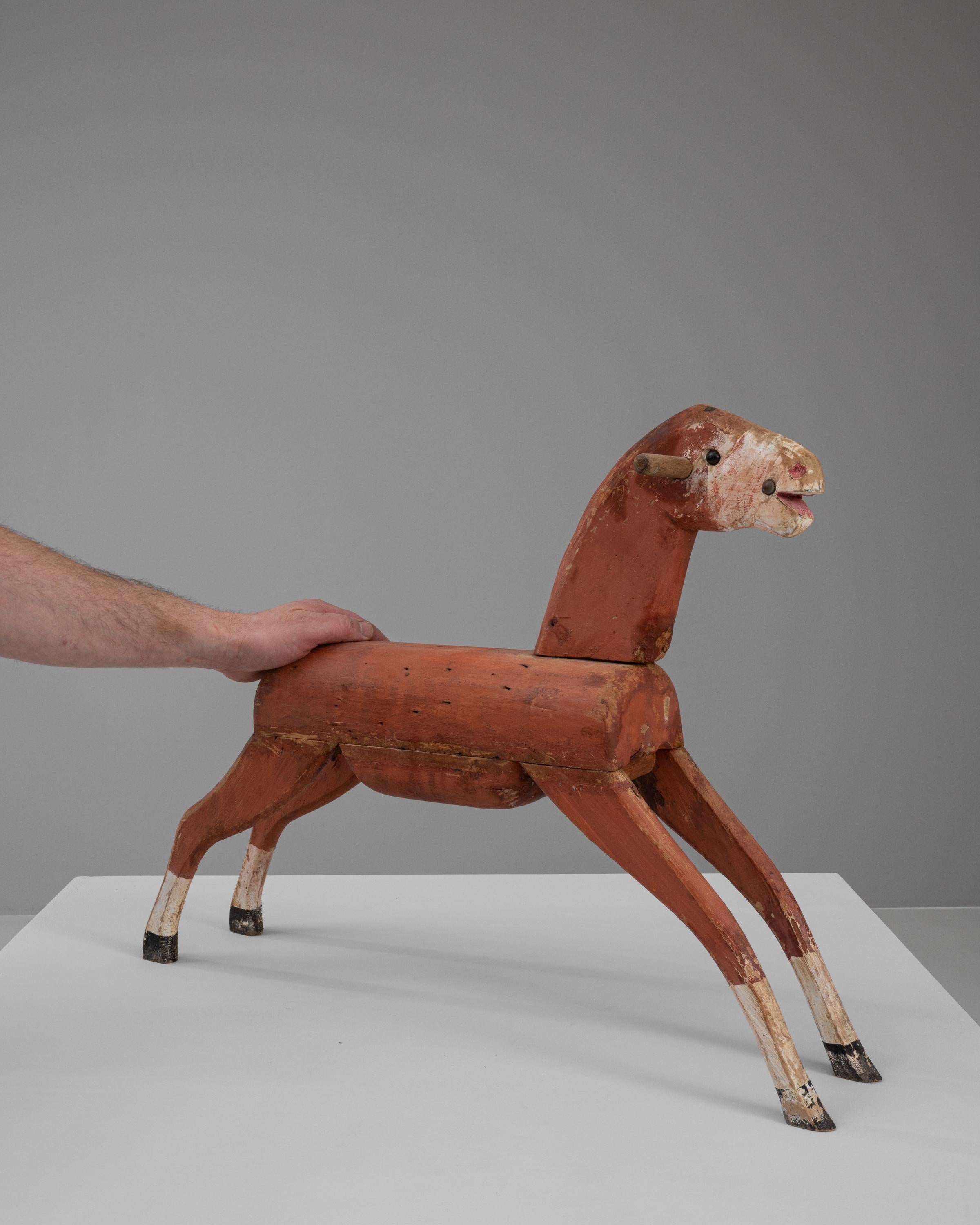 This Early 20th Century French Wooden Horse is a captivating piece of folk art, rich with rustic charm and historical character. Crafted from wood and painted in a warm, earthy red with natural wear and patina, it exudes a sense of nostalgia and