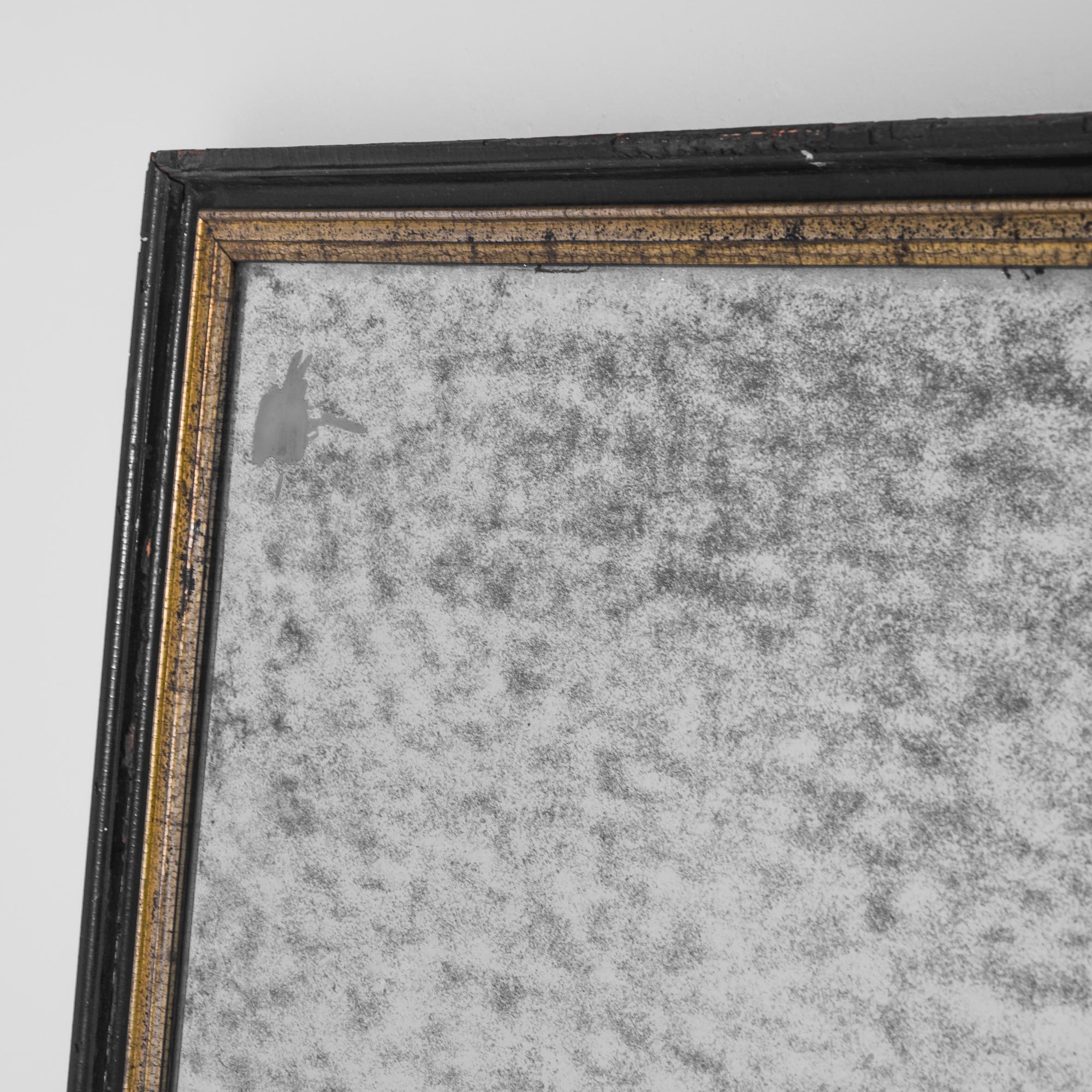 Black over gold — this looking glass, crafted in France circa 1900, features a classical black frame with a faded gold leaf adorning its inner part. The smoky texture of the surface, a graceful mark of time that adds a unique quality to this vintage