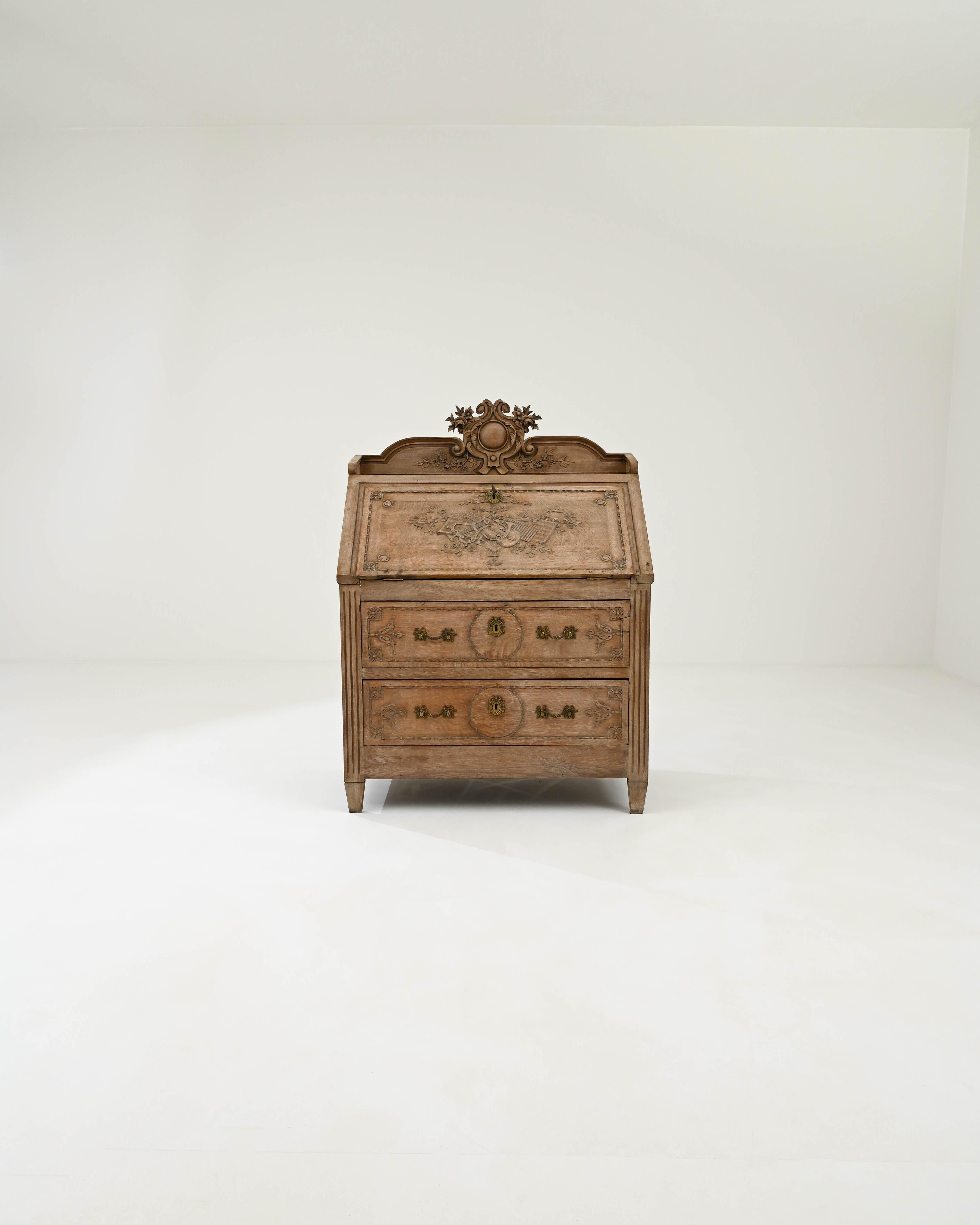A wooden desk created in early 20th century France. A crest of musical instruments and vines is proudly engraved into the center of this illustrious desk, framed in by a series of floral and scroll motifs. A delicate bleaching process has been