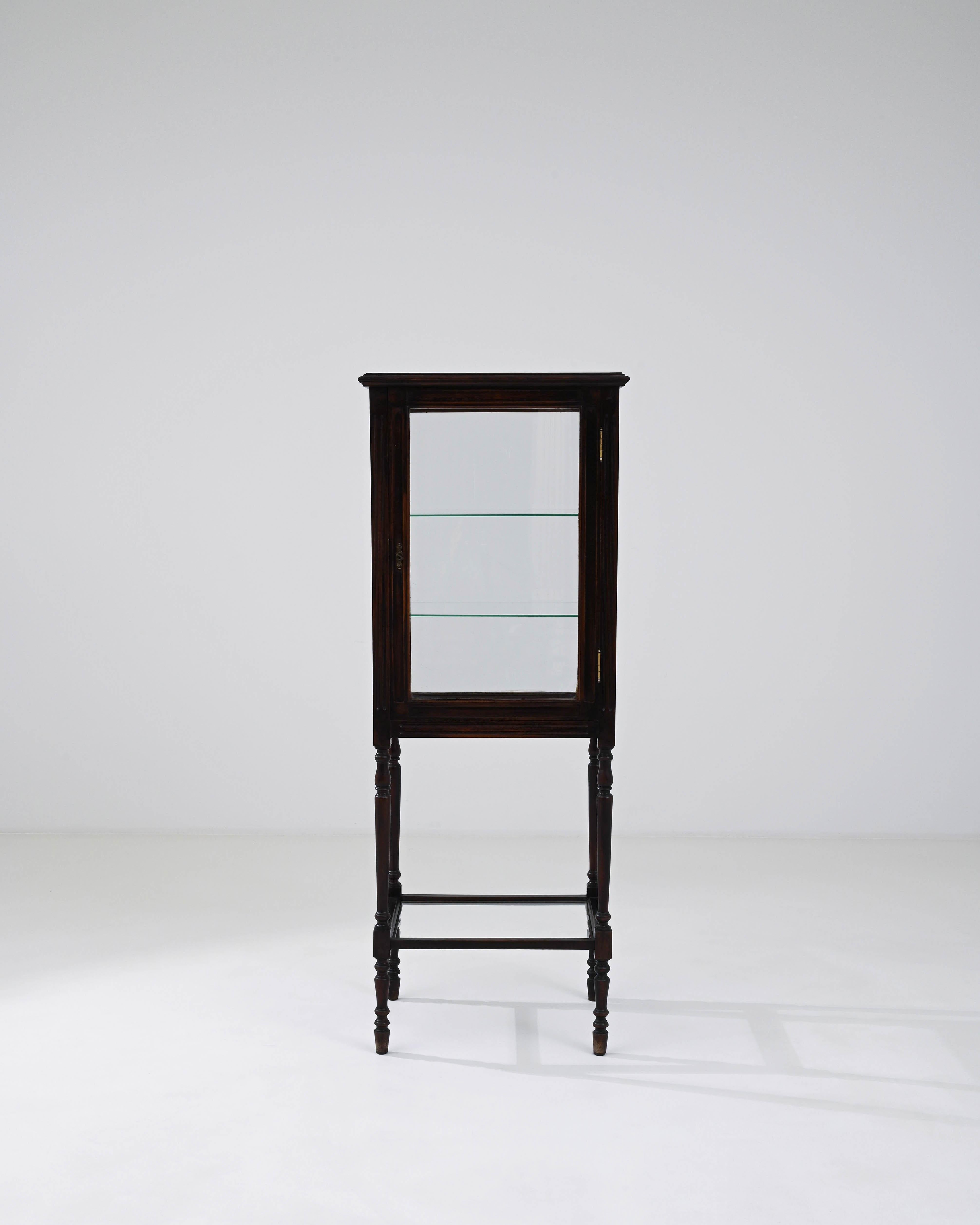 Step into the past with this exquisite Early 20th Century French Wooden Vitrine, a piece that exudes both charm and history. Standing tall on elegantly turned legs, this vitrine's dark, polished wood boasts the rich, deep hues of its storied life.
