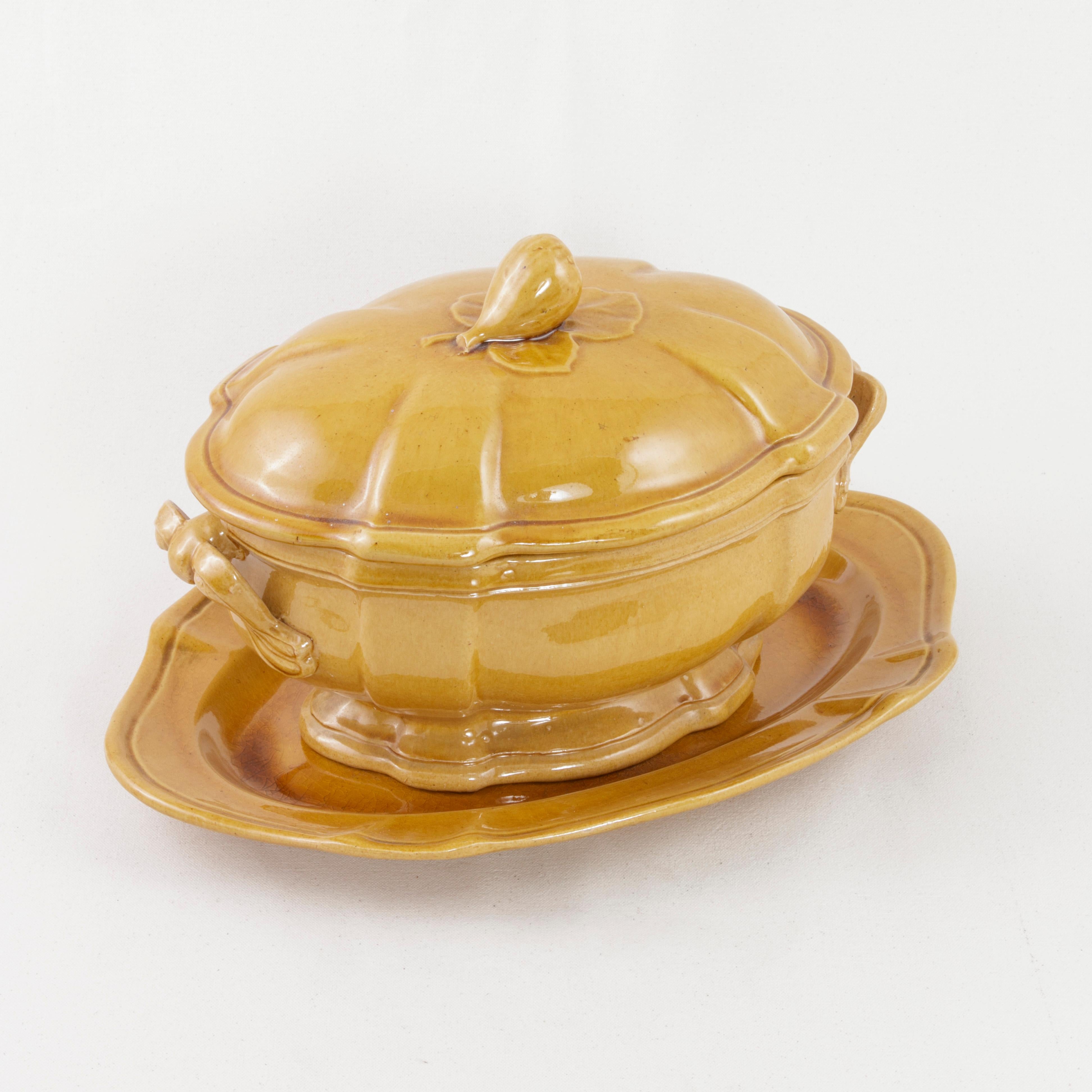 This early 20th century yellow faience soup tureen from the village of Uzès in the south of France, features its original lid and platter underneath. The lid is detailed with a fig and fig leaf handle. The tureen measures 8.75 inches in height, 12