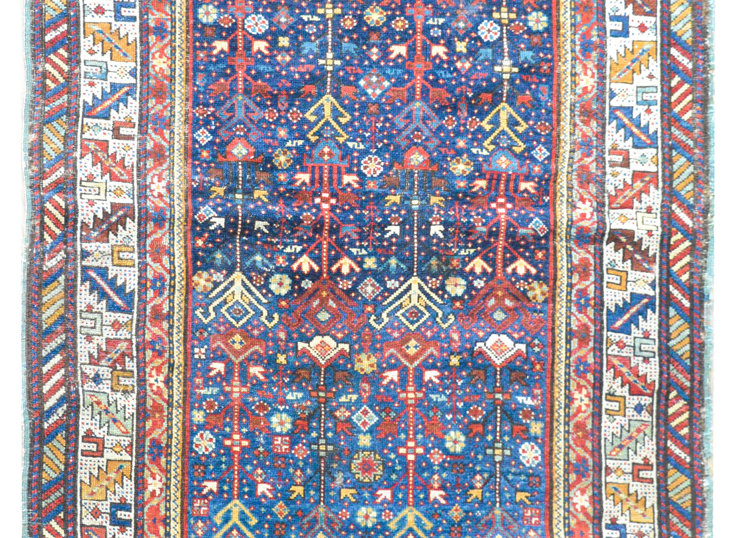 An outstanding early 20th century Persian Ganjeh rug with a fantastic stylized floral and vine pattern woven in bright crimson, gold, light indigo, and white set against an intensely woven field of flowers and all set against a dark indigo