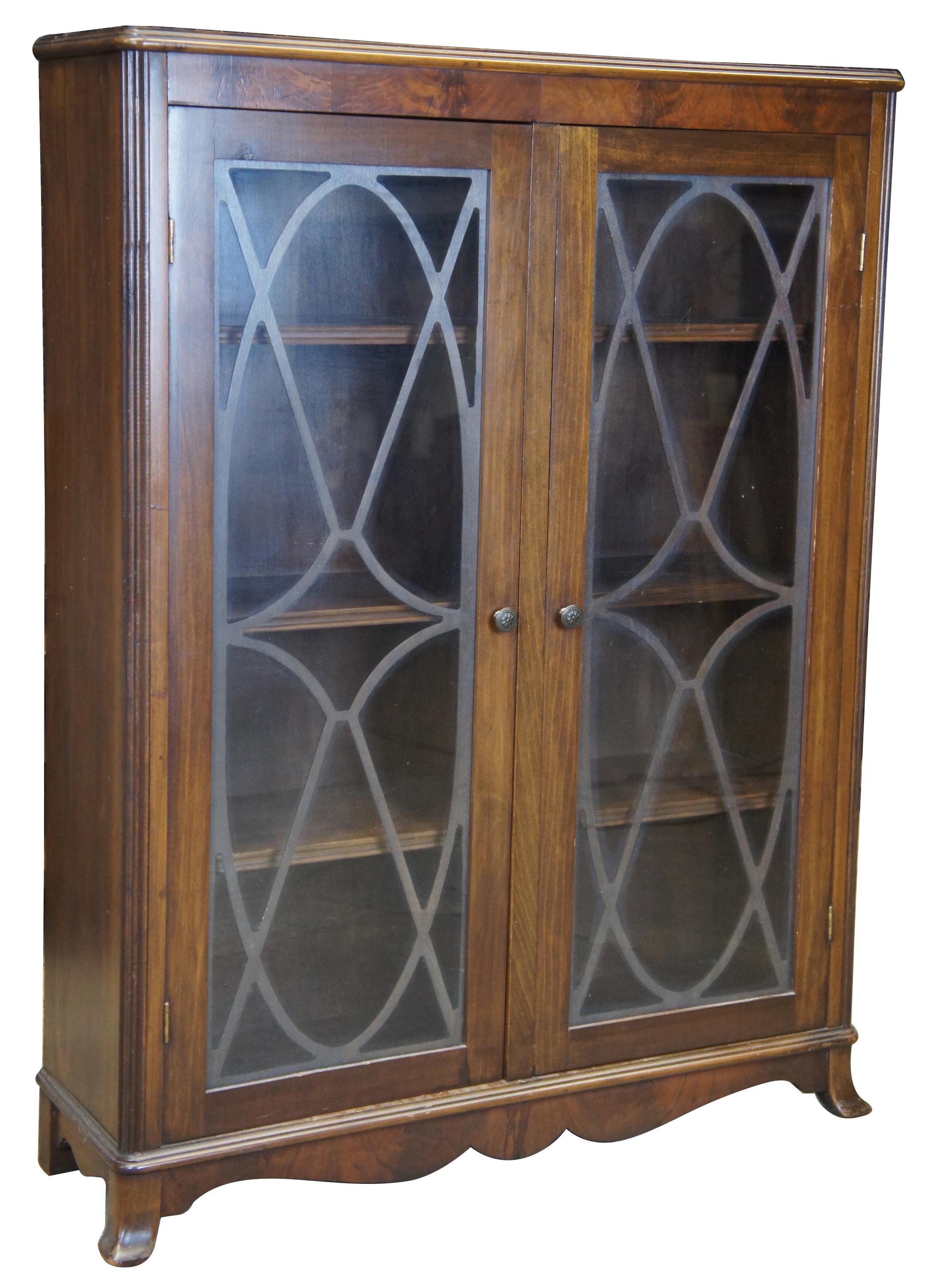 Georgian style walnut bookcase, circa 1930s. Features three fixed shelves behind two glass doors with fretwork. Includes carved lower apron and flared legs.
  