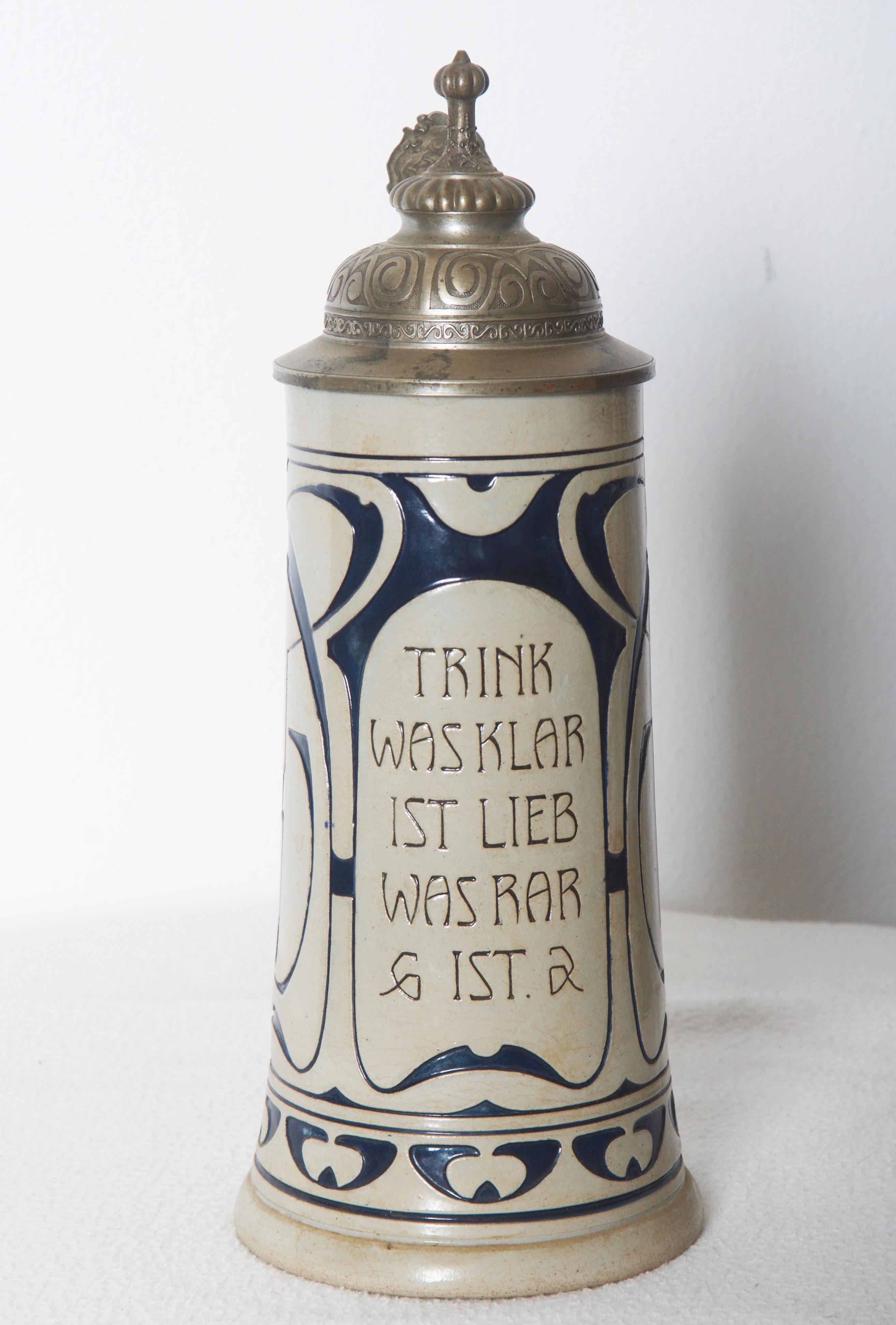 Stoneware 1/2l beer stein with an original pewter hinged lid. The body is decorated with a floral Art Nouveau ornaments.
Made in Germany.