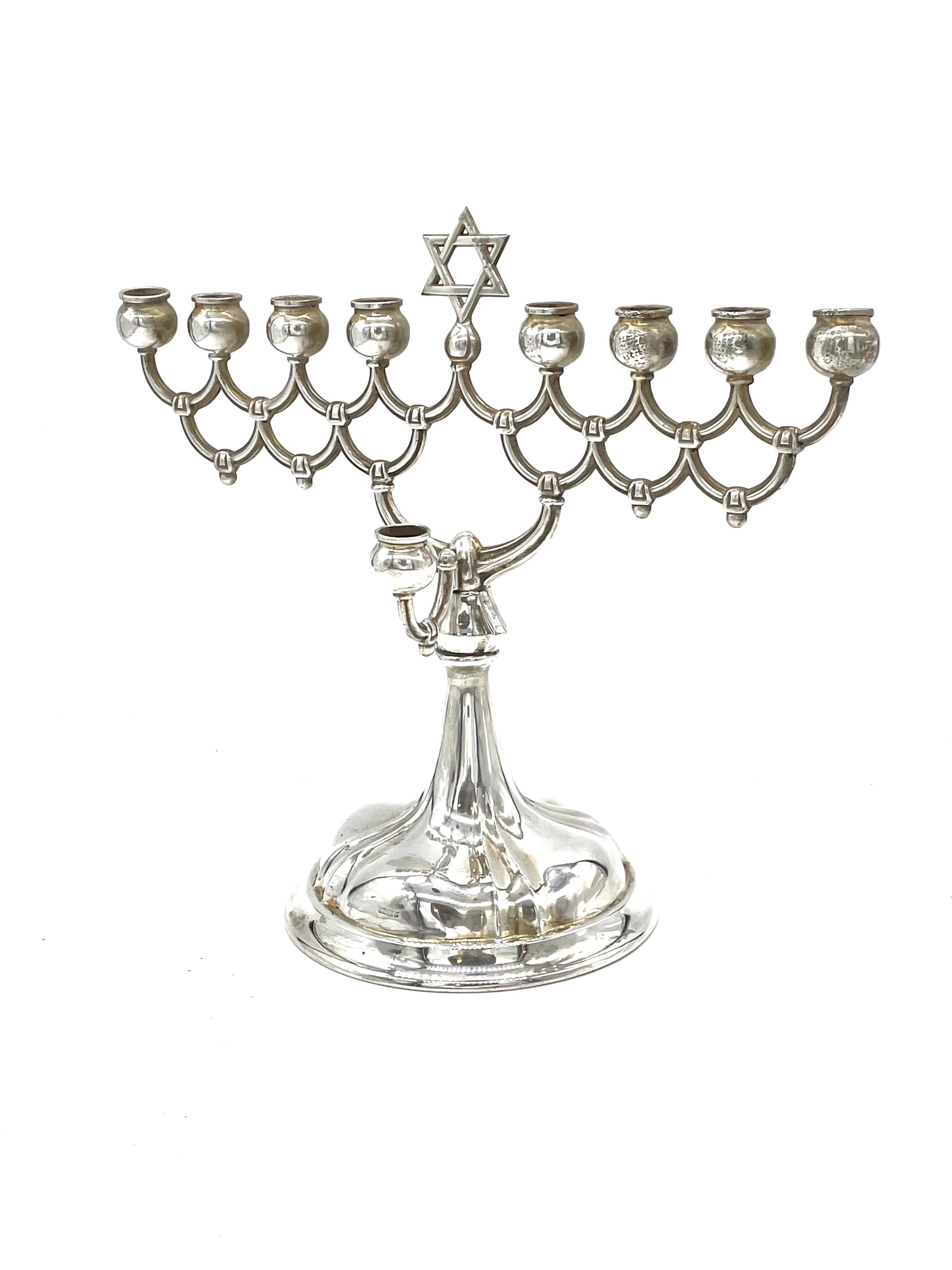 German silver Hanukkah lamp made in 1920’s features nine candleholders in traditional style. The round shaped candleholders are supported by tiers of concentric patterns. The harmonious toppling of arches with stylistic decoration is seen ornamented