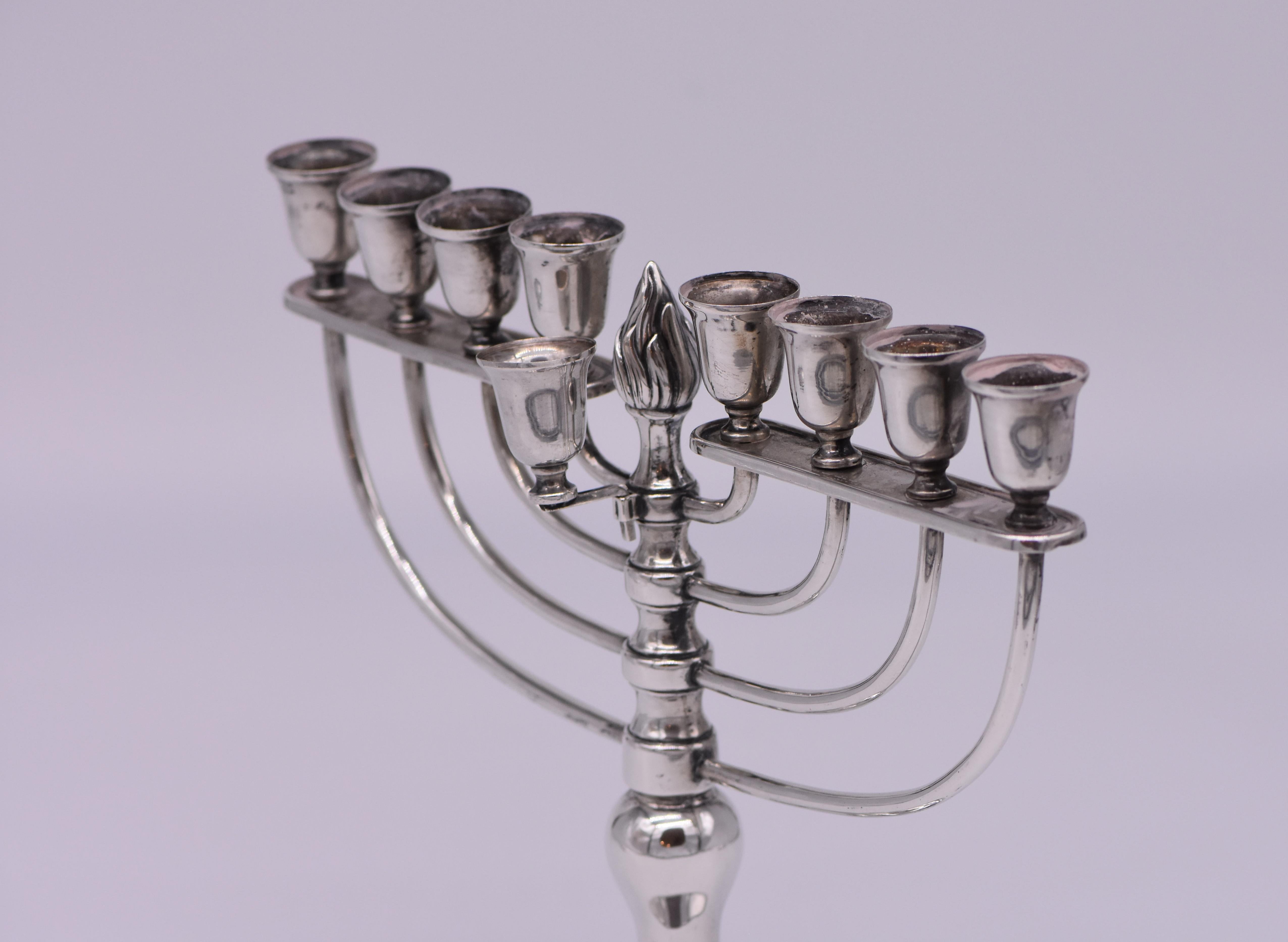 On round decorated base with baluster shape stem. 
The upper portion constructed with eight semicircle arms and original servant light.
Topped by a silver flame finial.
Marked with German silver hallmarks.

Every item in Menorah Galleries is