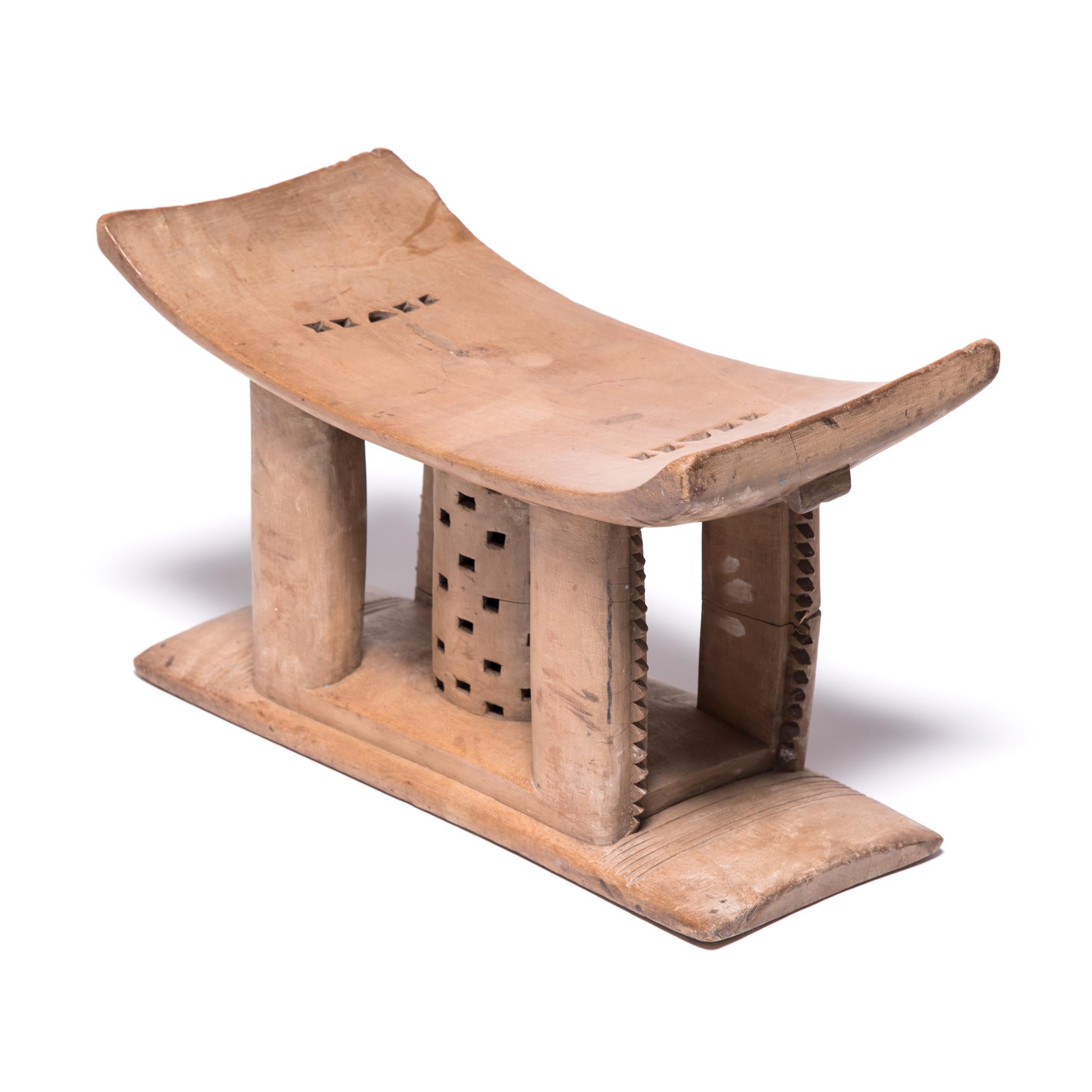 In traditional Ashanti culture, stools indicated power, status, and lines of succession. The flat base, curved seat, and ridged supports of this stool reference the Ashanti King stool. The central symbol is the cylindrical version of the Kete Pa, or