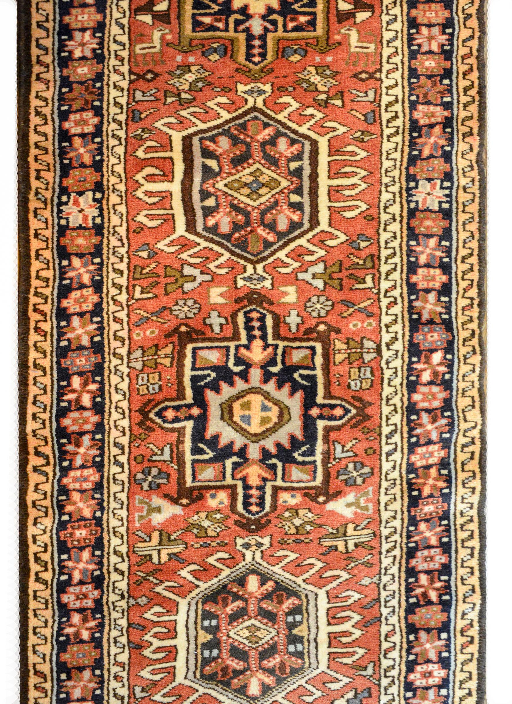 A wonderful early 20th century Persian Karadja runner with several stylized floral medallions woven in black, crimson, light blue, gold, and pale green amidst a field of more stylized flowers against a crimson background. The border is wonderful