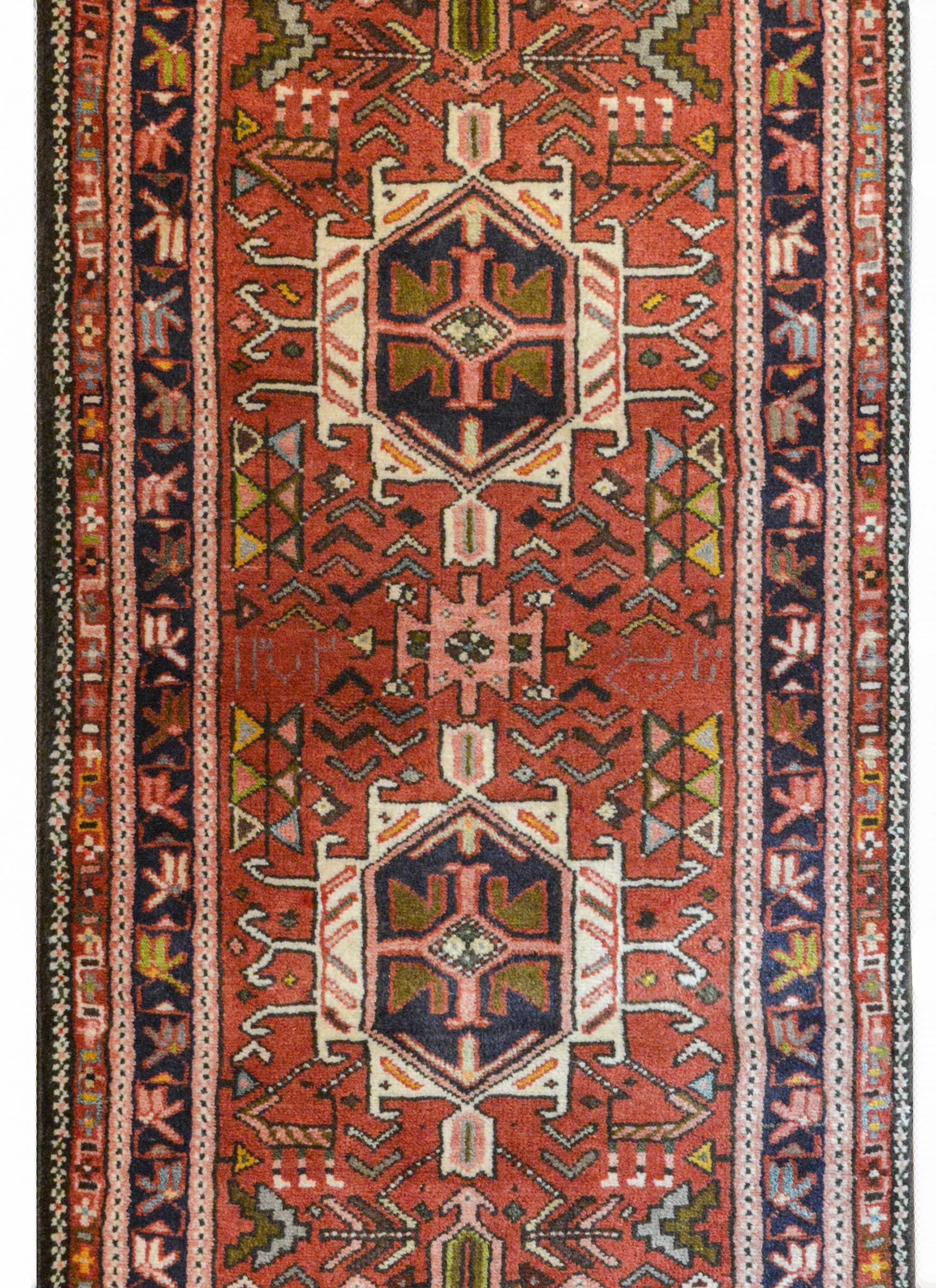 A wonderful early 20th century Persian Karadja runner with several stylized floral medallions woven in black, crimson, light blue, gold, and pale green amidst a field of more stylized flowers against a crimson background. The border is wonderful