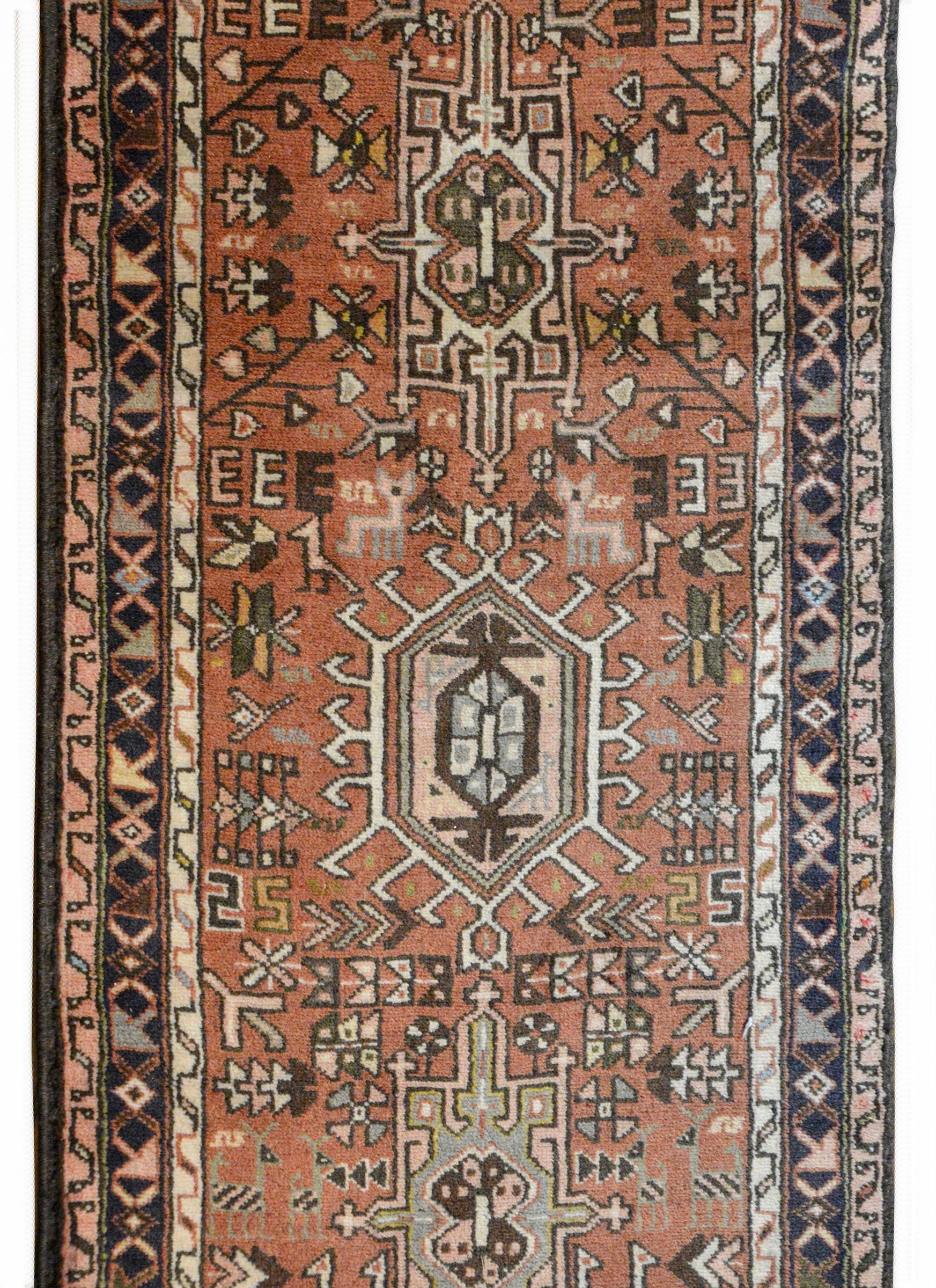 A wonderful early 20th century Persian Karadja runner with several stylized floral medallions woven in black, pink, light blue, gold, and green amidst a field of more stylized flowers against a burnt orange background. The border is wonderful