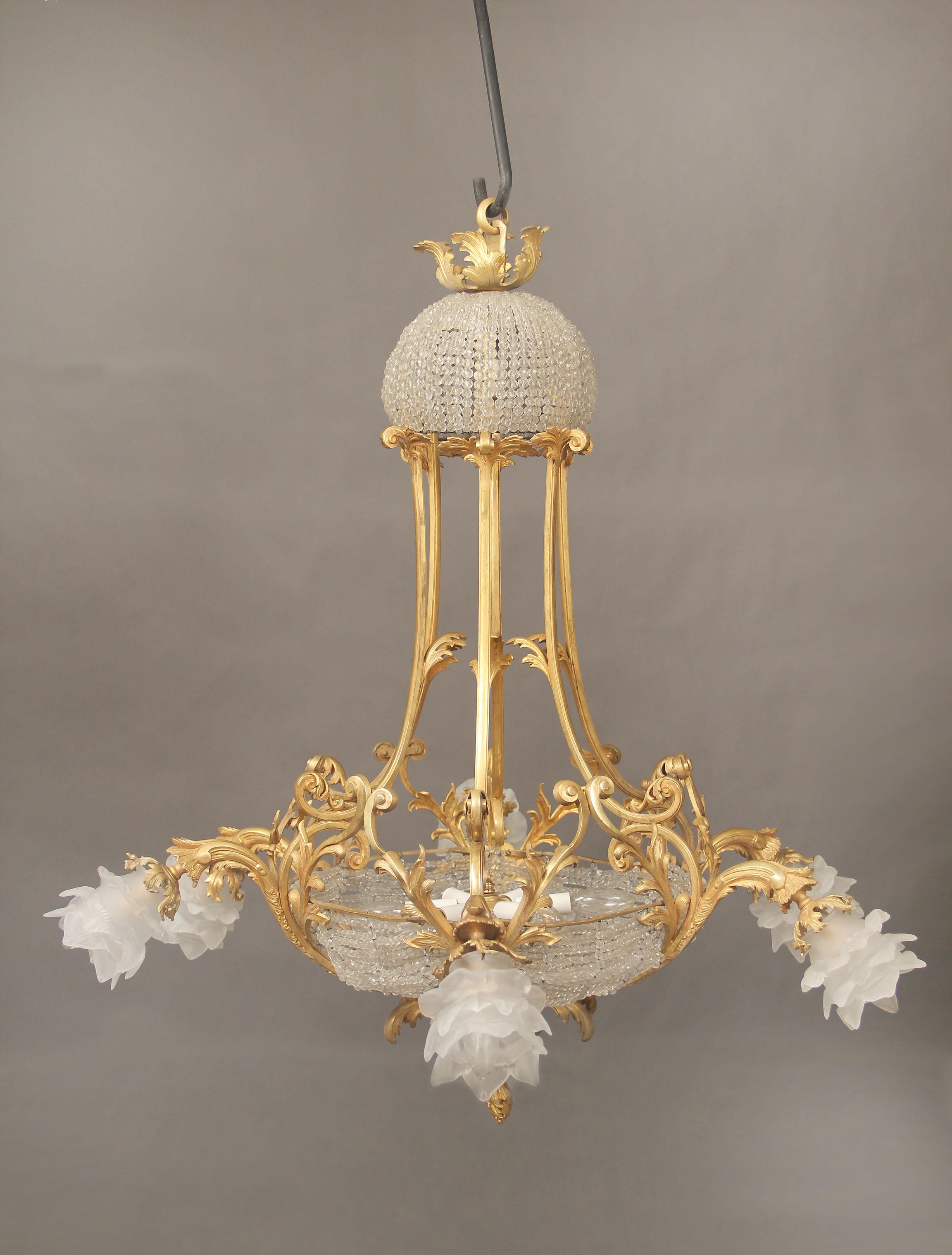 Lampadario a 13 luci con cesto di perline in bronzo dorato dei primi del Novecento

 Una corona con perline di cristallo e un fondo a cesto, sei luci perimetrali con paralumi a rosa, sei luci interne inferiori e una luce nella corona.
