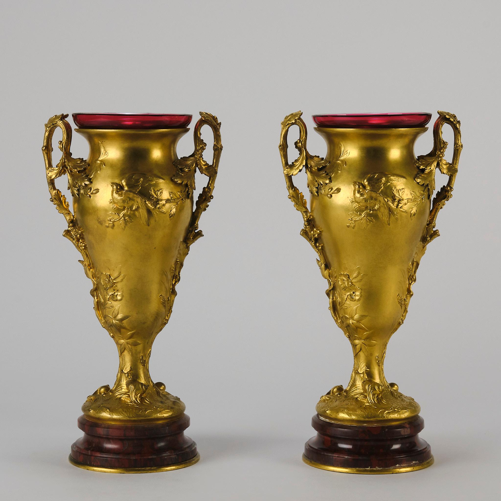 A highly attractive pair of late 19th century gilt bronze twin handled vases. The handles in the form of twisted vines and the vases decorated with butterflies and birds with snails around the bases. The tops complete with cranberry red glass