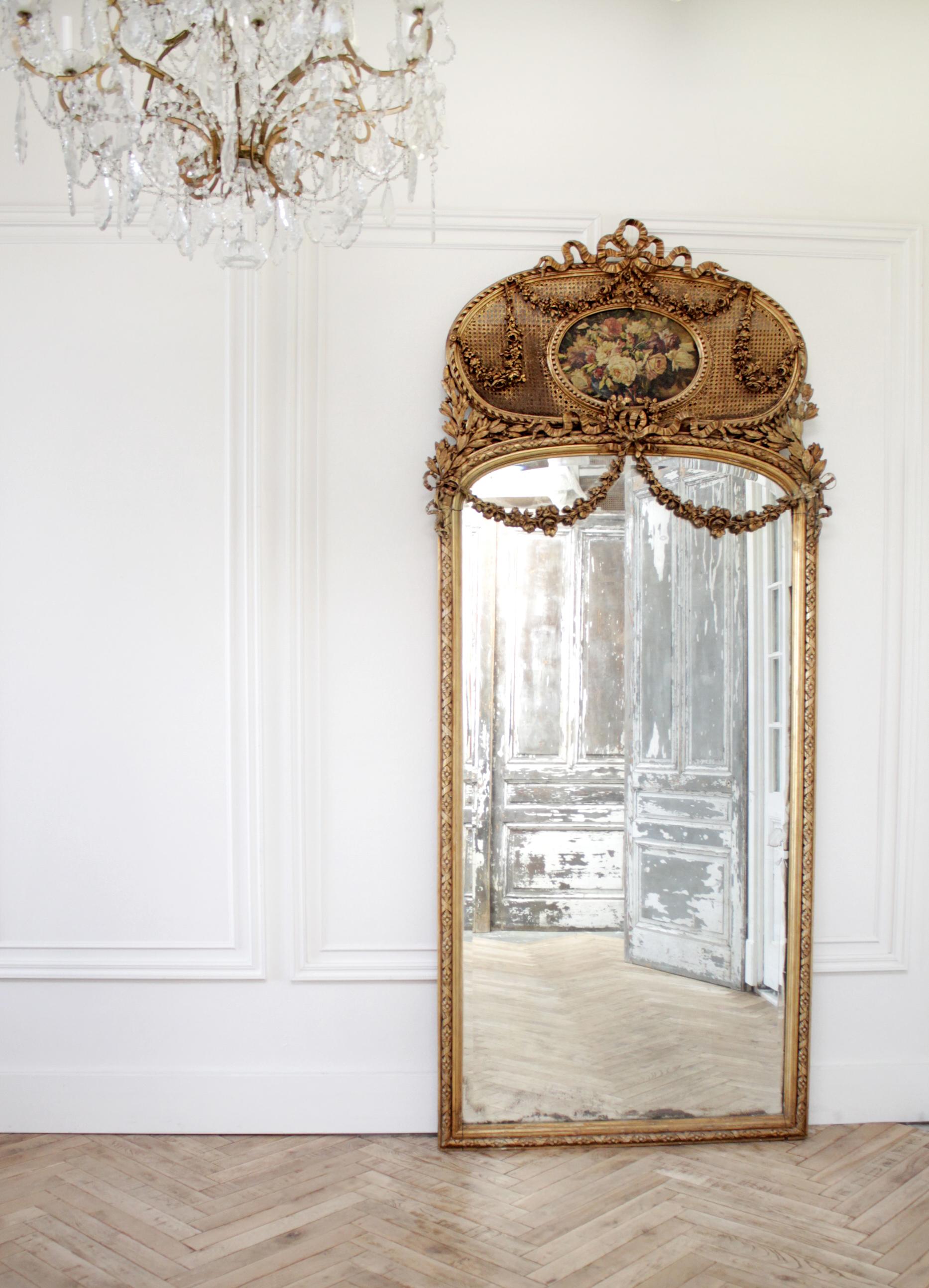 Early 20th century giltwood carved roses and cane trumeau mirror.
This beautiful tall trumeau has a hand painted roses on board, surrounded by large carved rose swags, and ribbons. Cane is in good condition. The mirror is original and shows signs