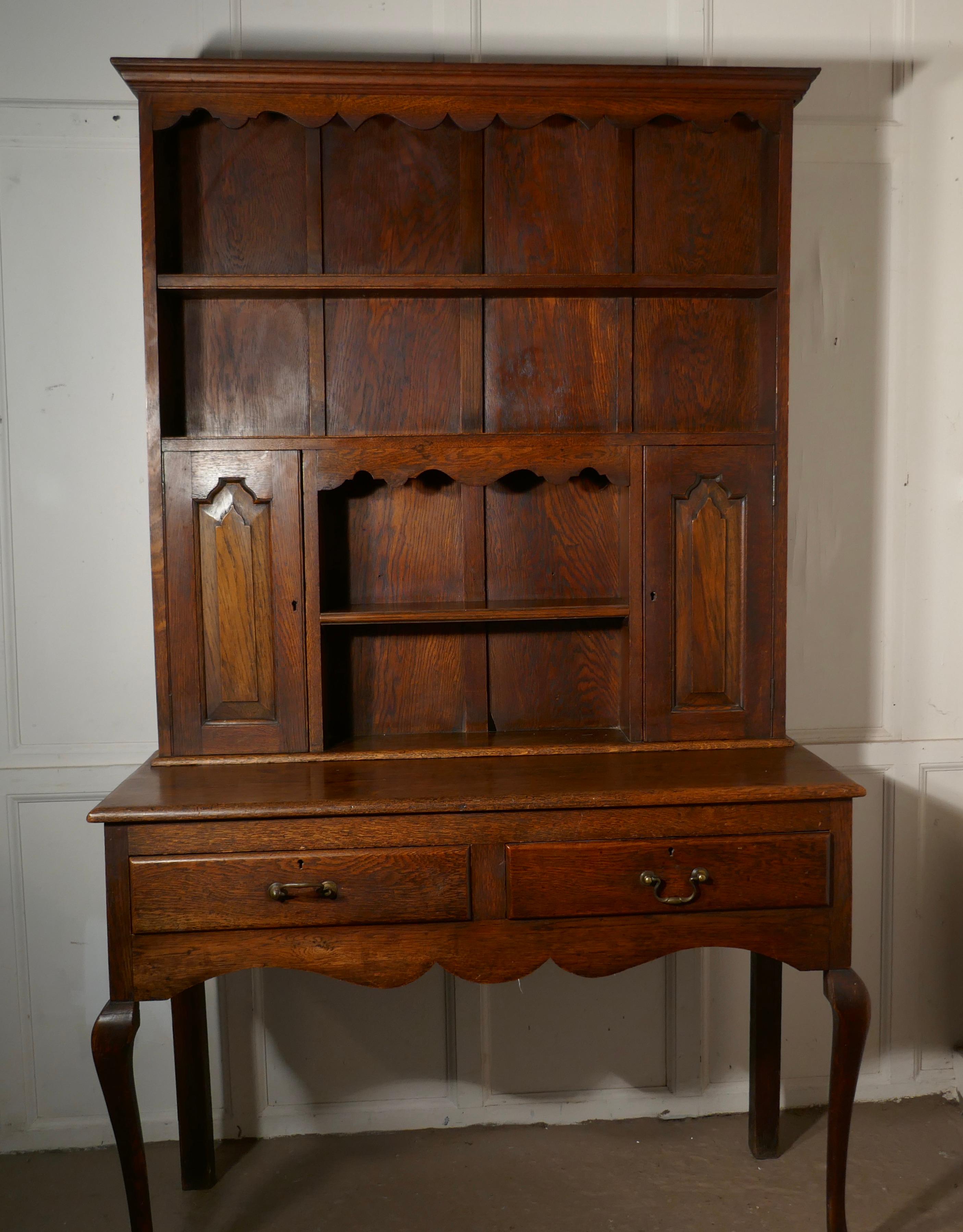 Early 20th century Gothic golden oak welsh dresser

The dresser has a shelved top beneath the long plate shelf below there are 2 cupboards one at each side with a shorter shelf in the middle, the shelves all have plate rails
The top cornice and