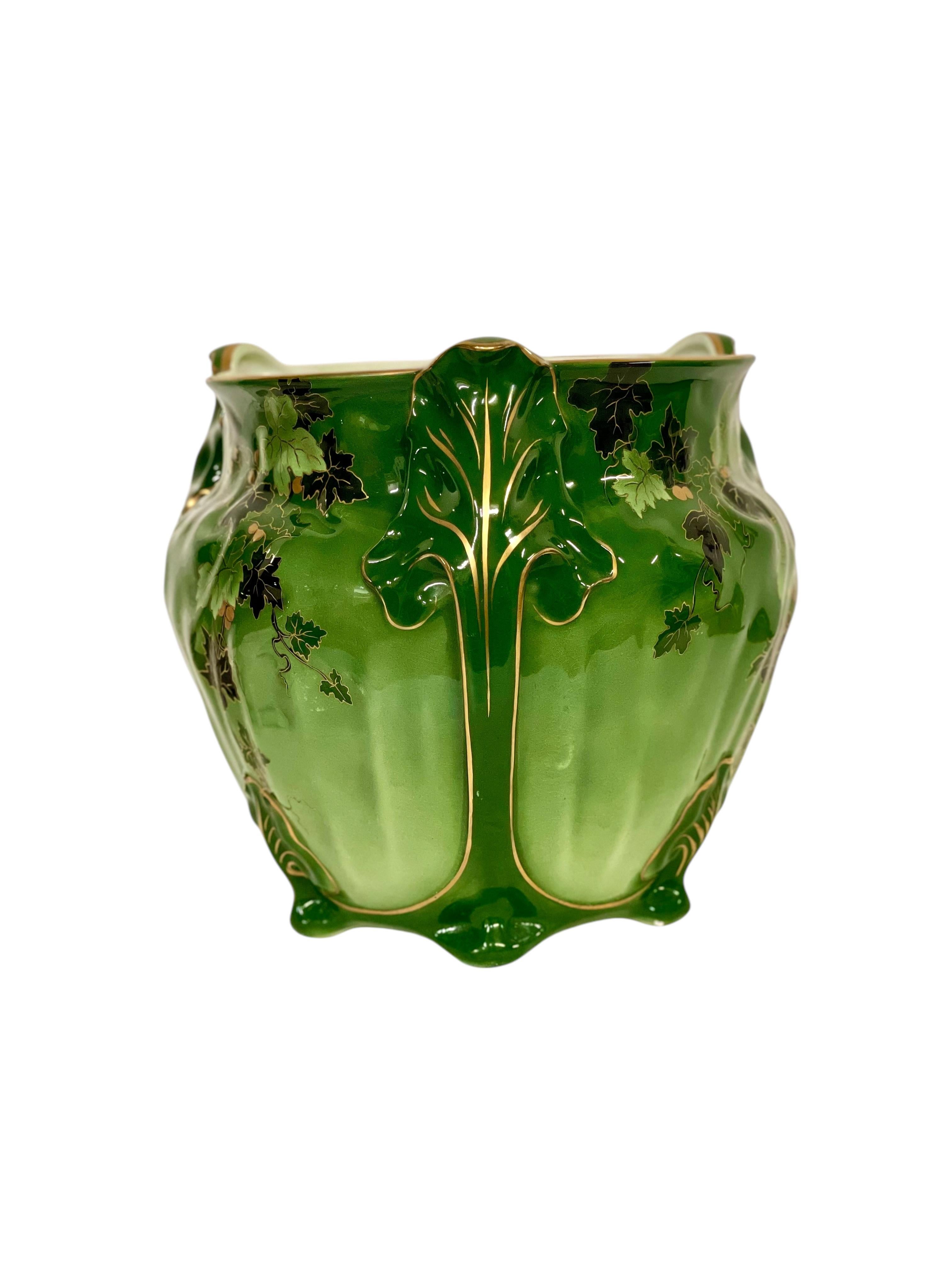 Ce superbe cache-pot Art nouveau illustre l'élégance et la créativité des arts décoratifs du début du XXe siècle. Son émail vert vibrant est orné d'un délicat motif de vigne peint à la main, avec des feuilles de lierre entrelacées dans des tons de