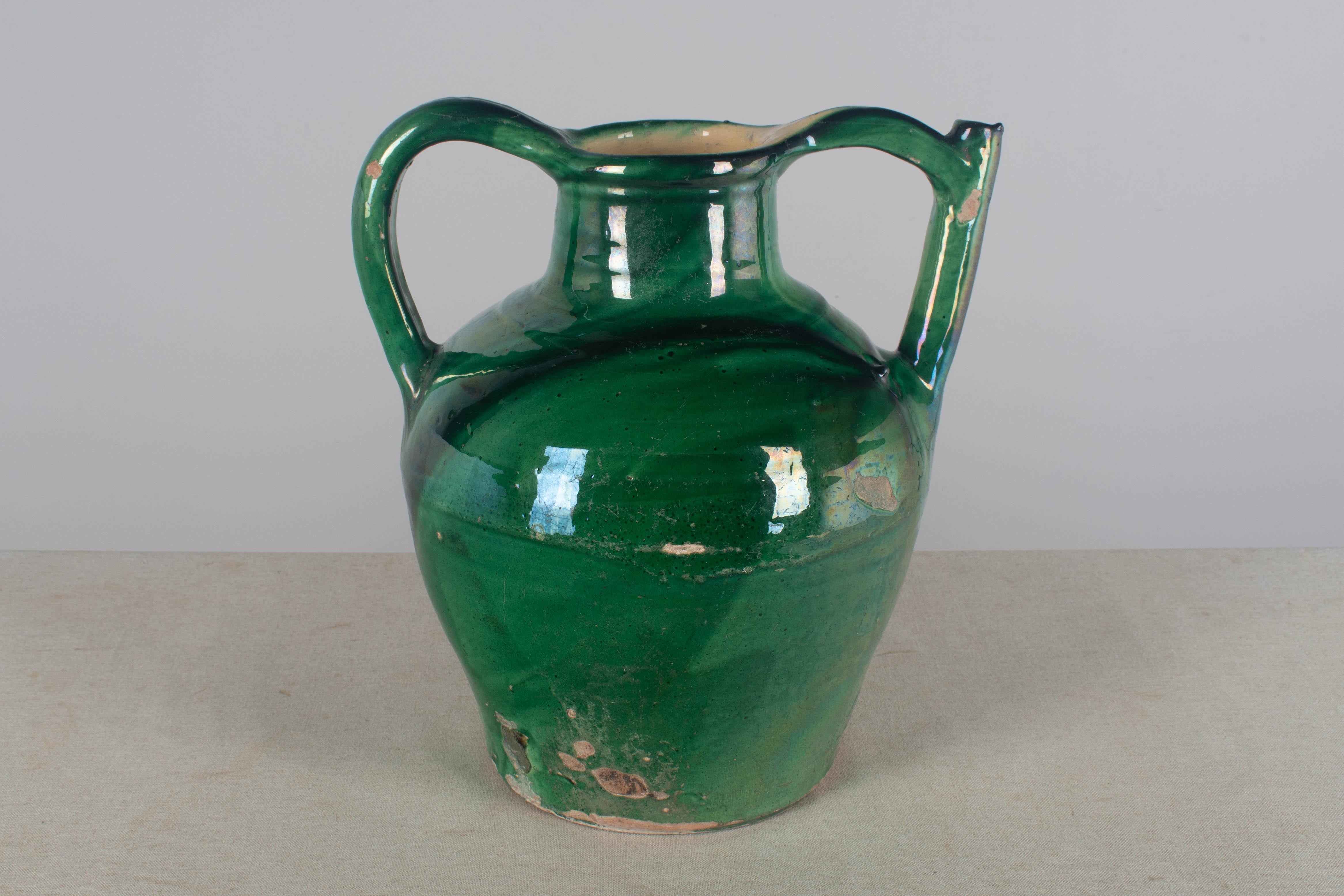 An early 20th century green glazed terracotta vinegar or water jug from the Southwest of France with spout in the handle. Beautiful green color. Chips and losses to glaze. Circa 1900s. Dimensions: 14