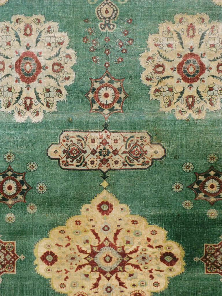 An antique Indian Agra carpet with a weathered appeal from the early 20th century. In the Persian Sultanabad-Mahal style, but with a green field instead of madder red, the gently scalloped straw central medallion pends cartouches and palmettes,