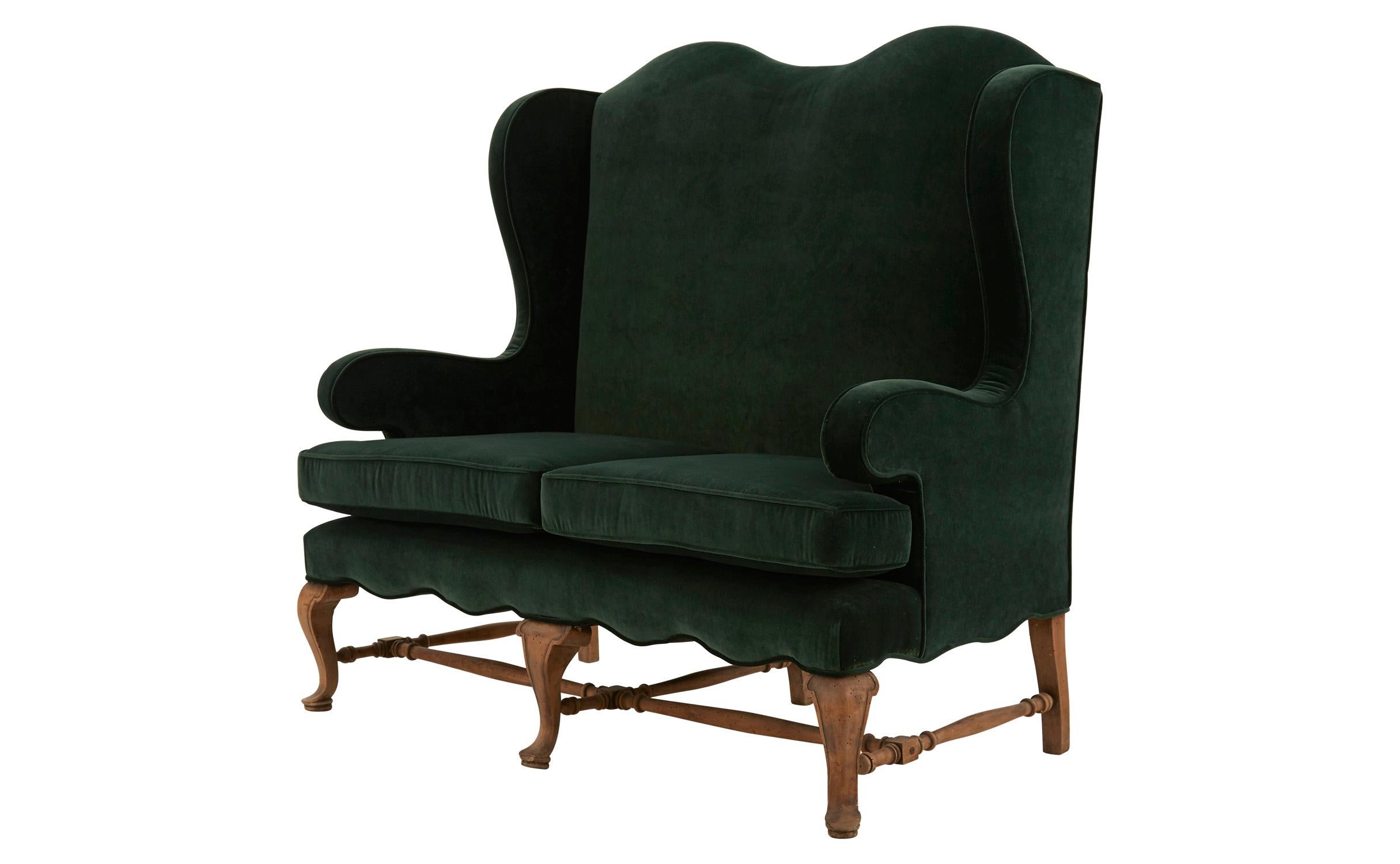 Our Antique Spanish Settee was crafted in Spain in the early 20th century. We’ve given this classic high-backed frame a fresh feel, reupholstering it in sumptuous emerald green velvet. This updated touch pairs nicely with its stripped wood base and