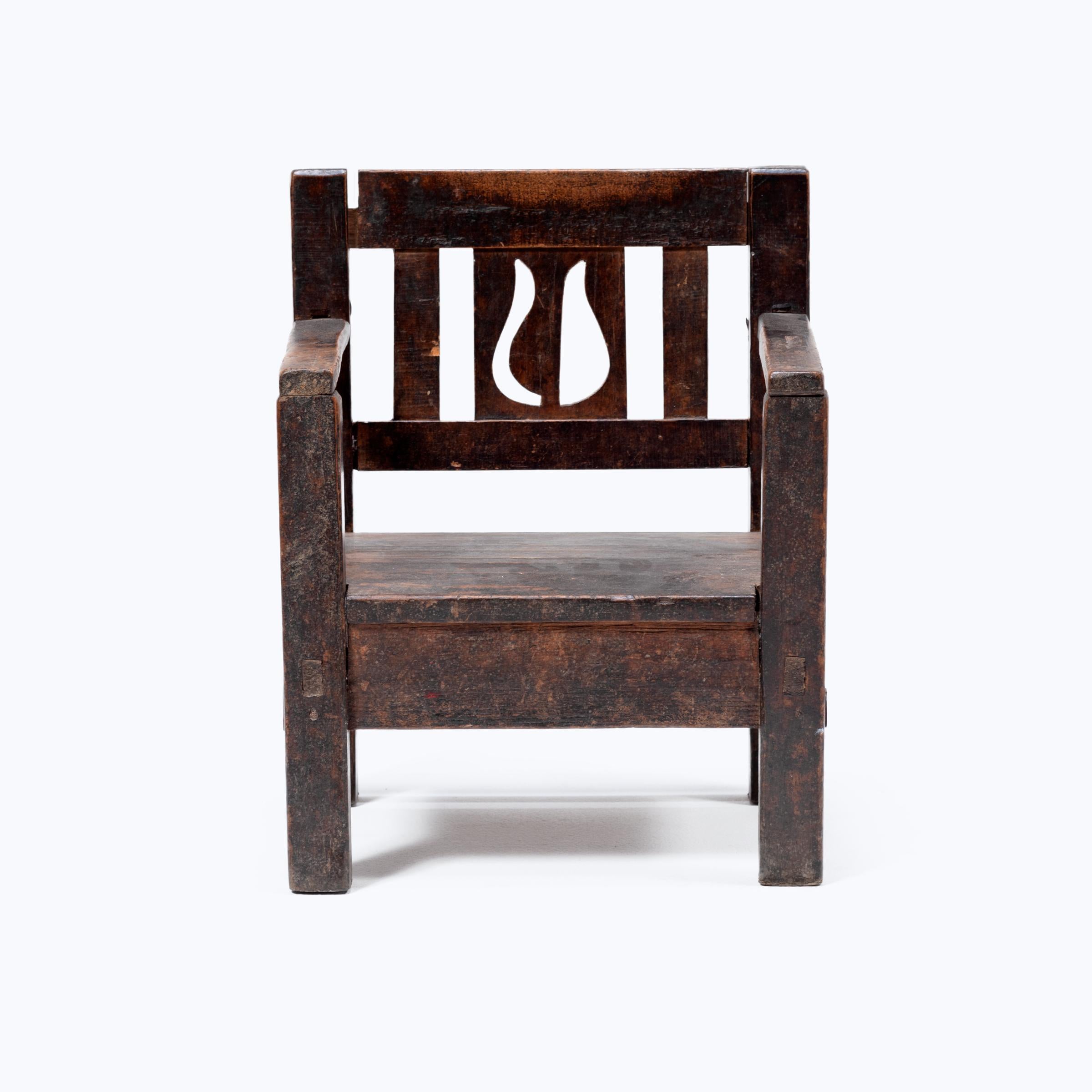Crafted in the early 20th century, this petite Guatemalan children's chair charms with its playful asymmetry and richly textured surface. Influenced by Spanish Colonial furniture design, the chair has a slatted back carved with an abstract flower
