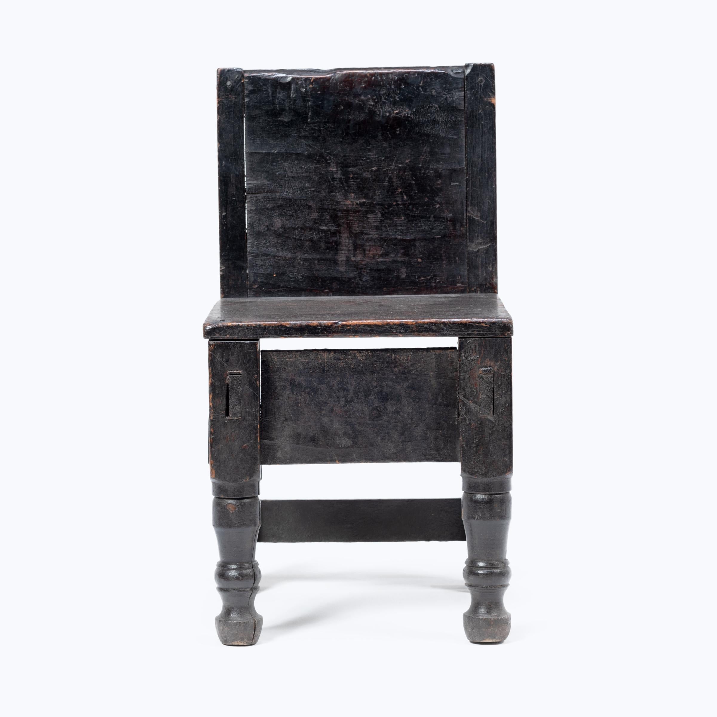 Dieser zierliche guatemaltekische Kinderstuhl aus dem frühen 20. Jahrhundert besticht durch seine verspielte Asymmetrie und die Mischung der Motive. Der bemalte Stuhl mit seiner kantigen Rückenlehne und dem quadratischen Sitz, der auf zwei