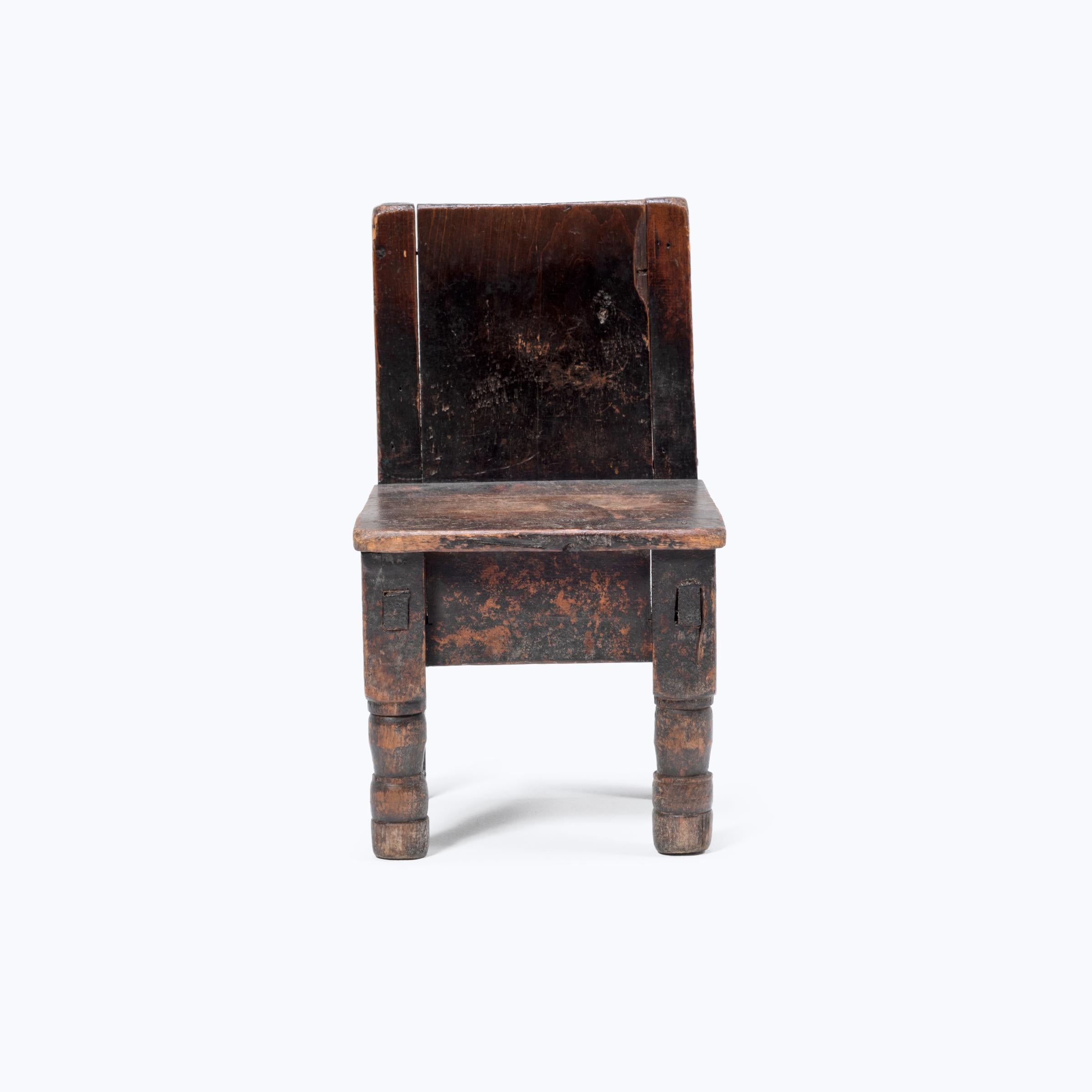 Crafted in the early 20th century, this petite Guatemalan children's chair charms with its playful asymmetry and richly textured surface. Influenced by Spanish Colonial furniture design, the chair has an angular back and square seat resting on two