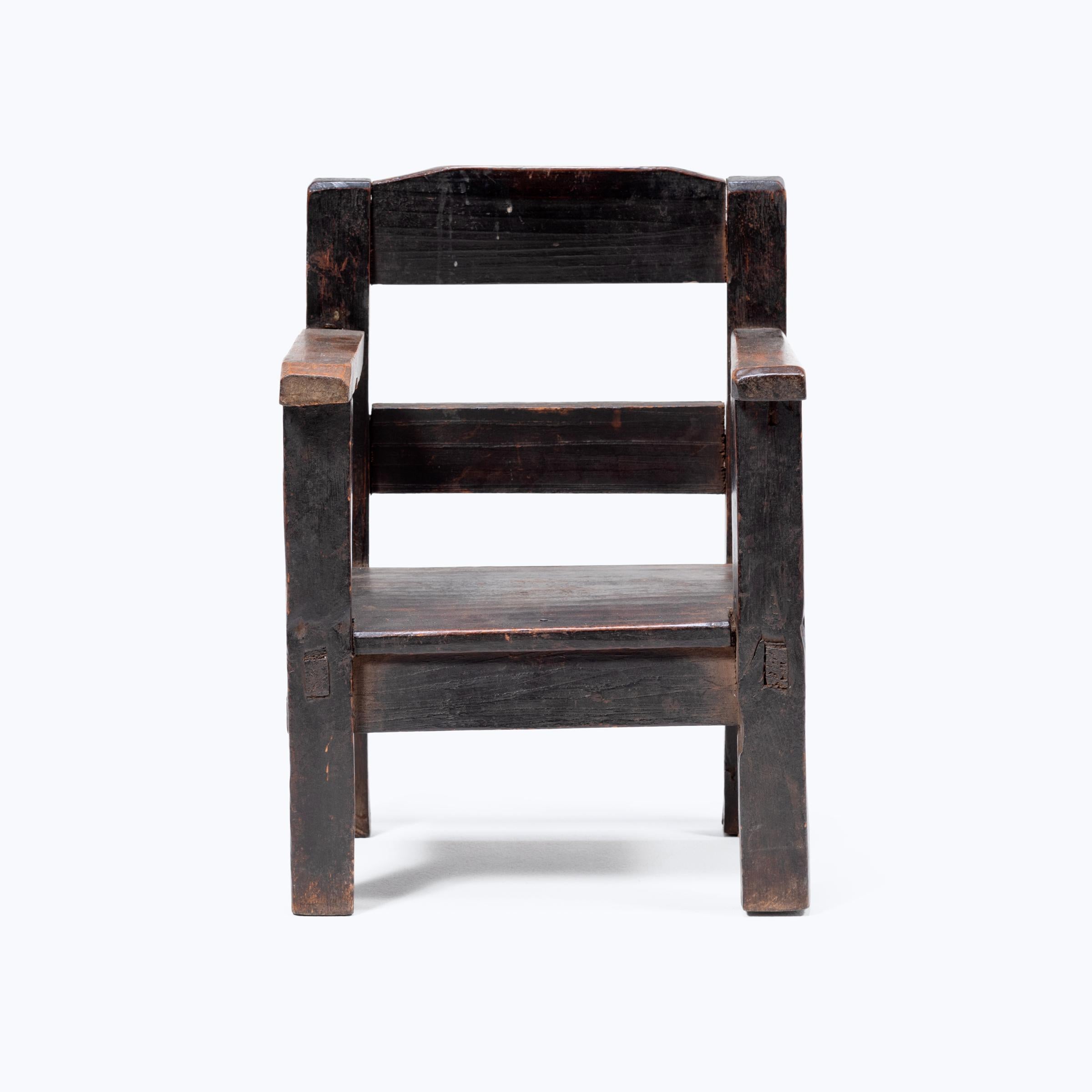 Crafted in the early 20th century, this petite Guatemalan children's chair charms with its playful asymmetry and richly textured surface. Influenced by Spanish Colonial furniture design, the chair has a slatted back and square seat framed by two